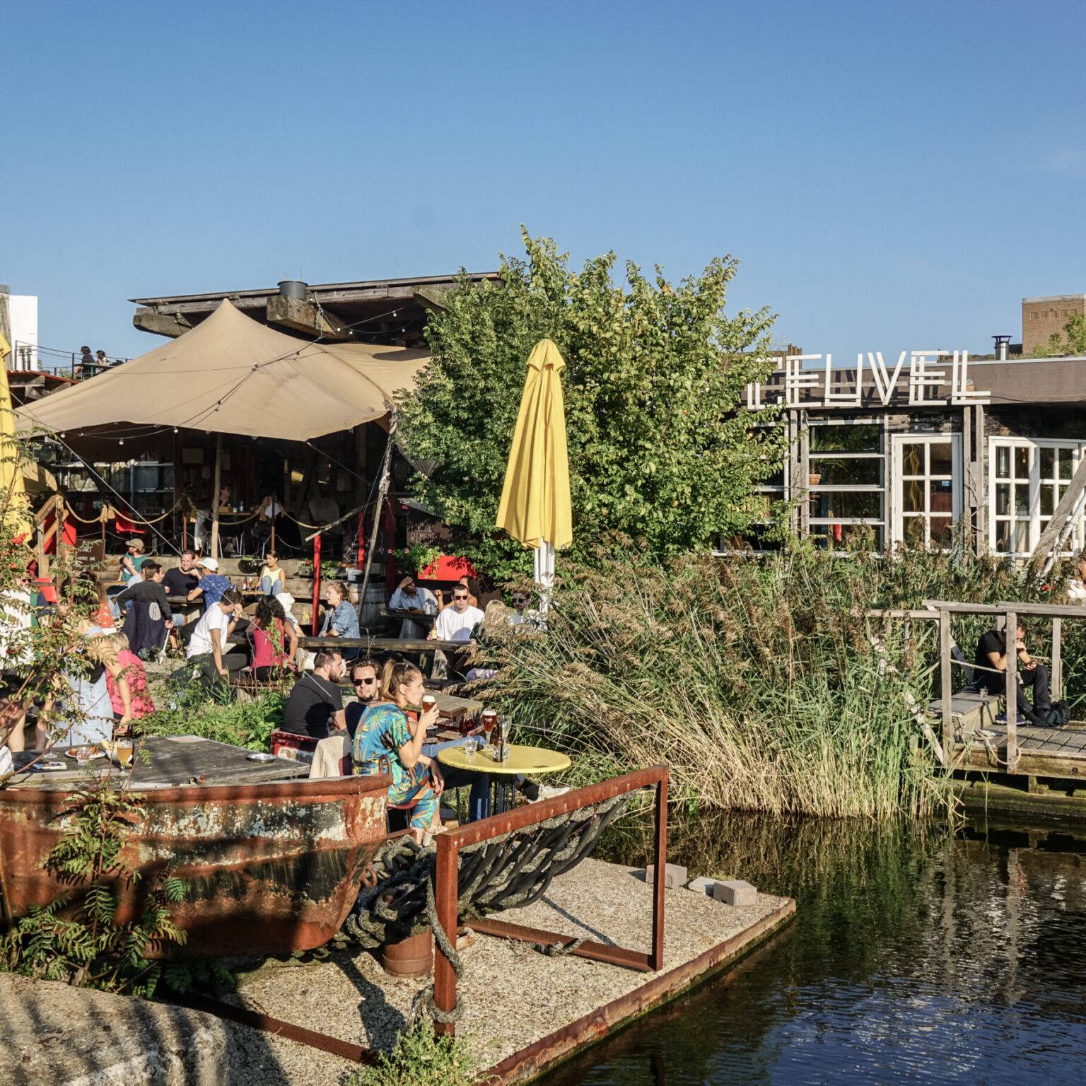 Die voll besetzte Terrasse des Café De Ceuvel direkt am Wasser und mit vielen Pflanzen.