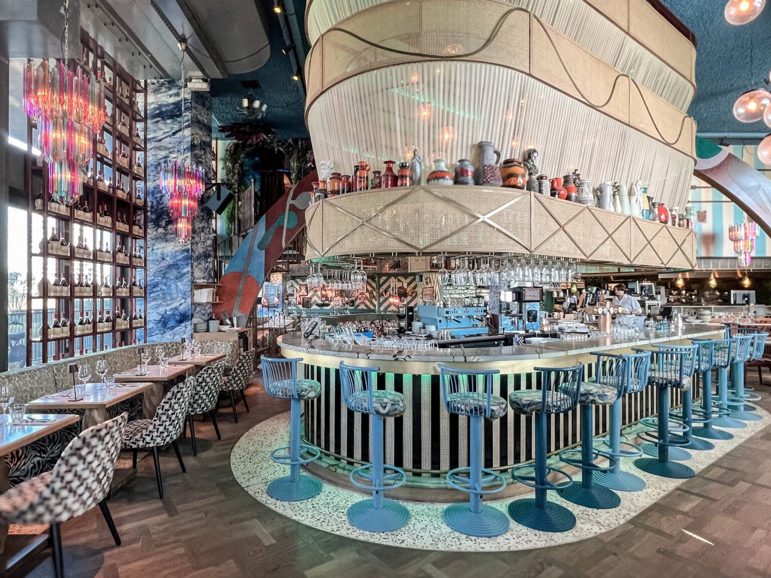 Bunter Gastraum mit stylischer Bar im Restaurant Gio’s by the River in Amsterdam-Noord, eingerichtet mit farbenfrohen Möbeln und dekorativen Details.