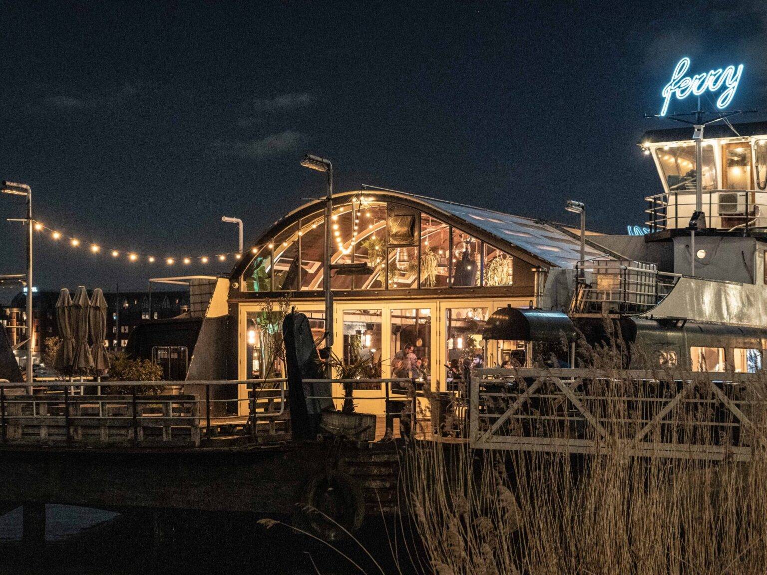 Das Restaurant Ferry von außen bei Nacht mit Lichterketten und einem großen blauen Neon-Schild.