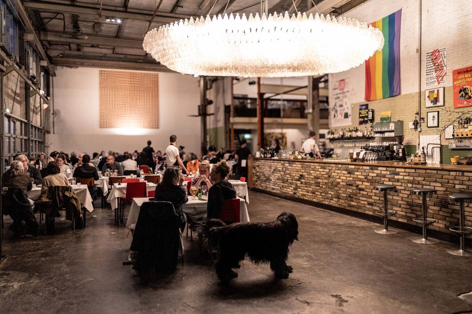 Innenansicht des Restaurants Hotel de Goudfazant in Amsterdam-Noord mit industriellem Ambiente, hohen Decken und riesigem Kronleuchter.