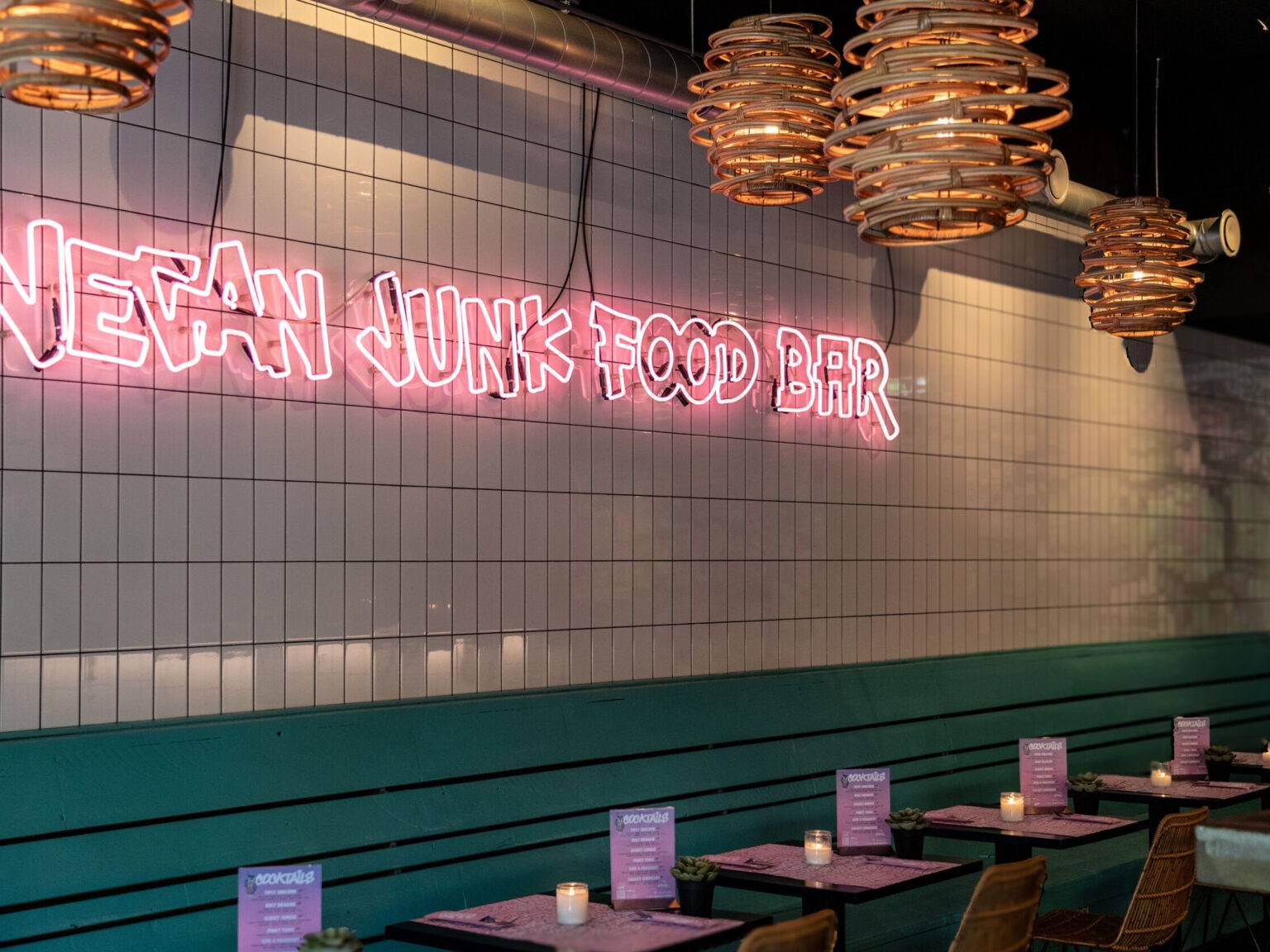 Innenansicht der Vegan Junk Food Bar in Amsterdam mit knalligem Interieur und leuchtendem Neon-Logo an der Wand.