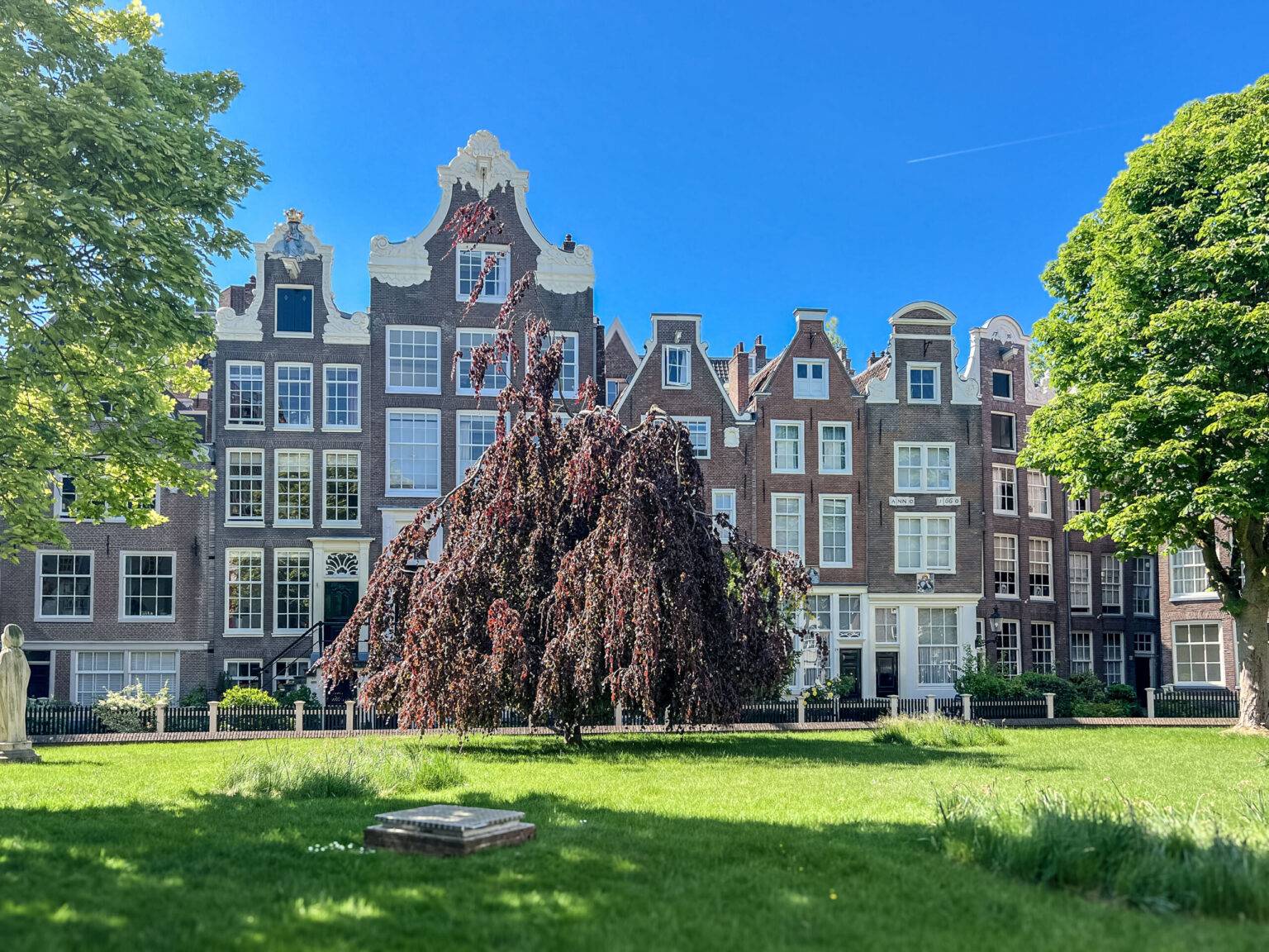 Idyllischer Blick auf den ruhigen Innenhof des Begijnhofs in Amsterdam mit historischen Häusern und gepflegtem Garten.