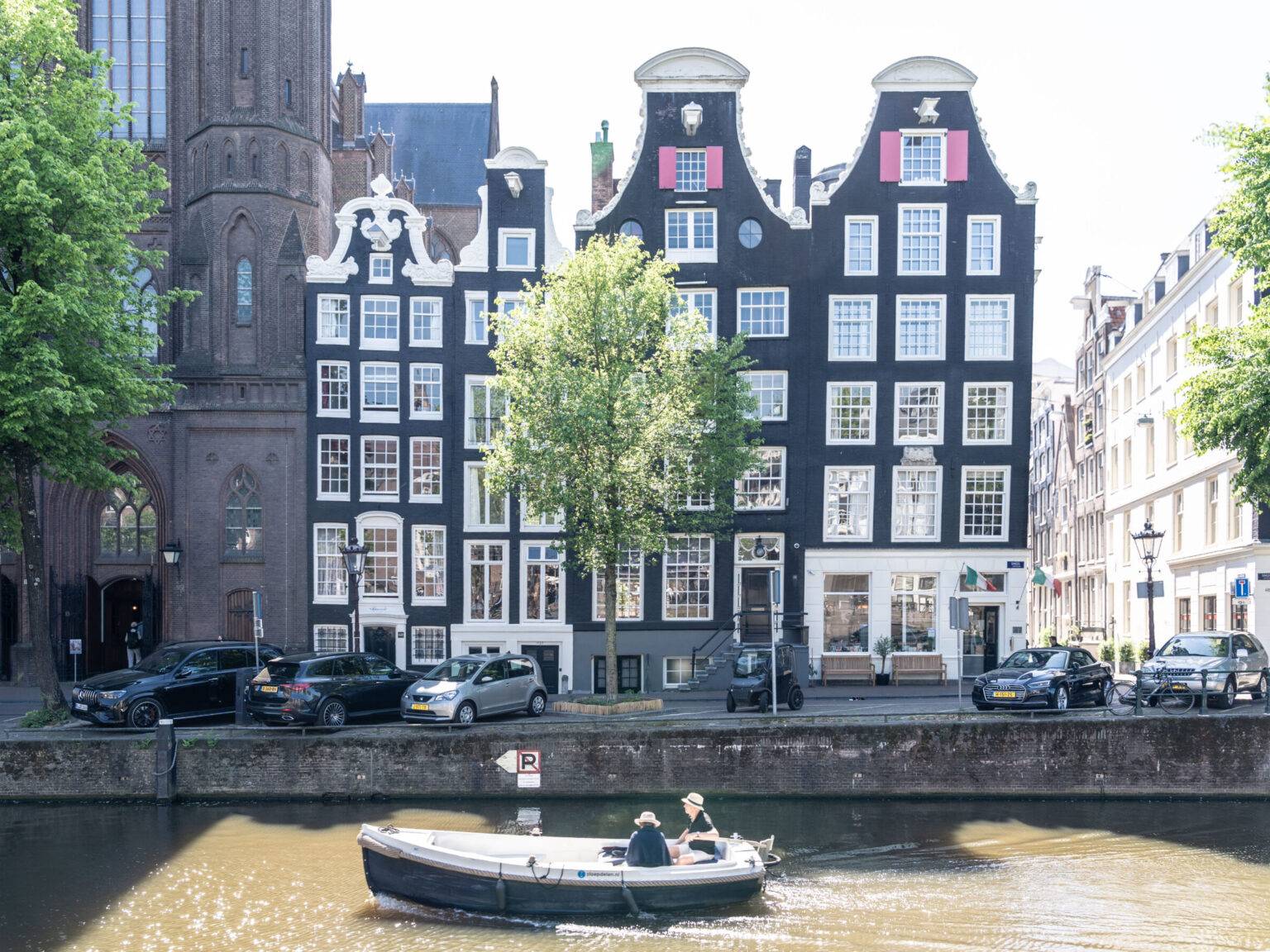 Zwei Personen in einem kleinen Boot fahren entspannt durch eine Gracht in Amsterdam, umgeben von typischer Stadtkulisse.