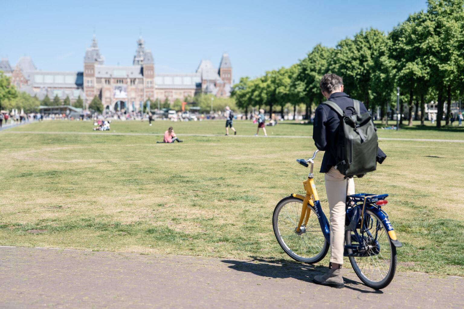 EIn Mann auf einem Fahrrad am Rande einer großen Rasenfläche.