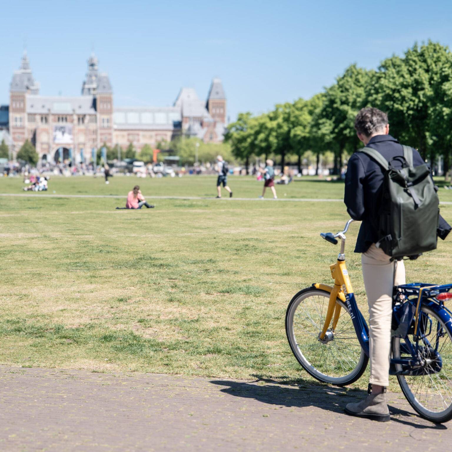 EIn Mann auf einem Fahrrad am Rande einer großen Rasenfläche.