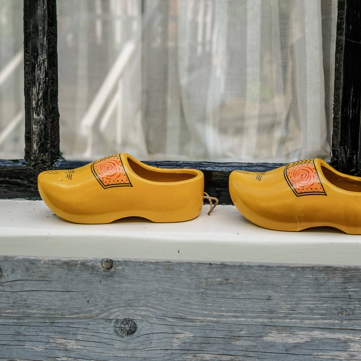 Zwei gelbe typisch niederländische Holzschuhe stehen auf einem Fenstersims.