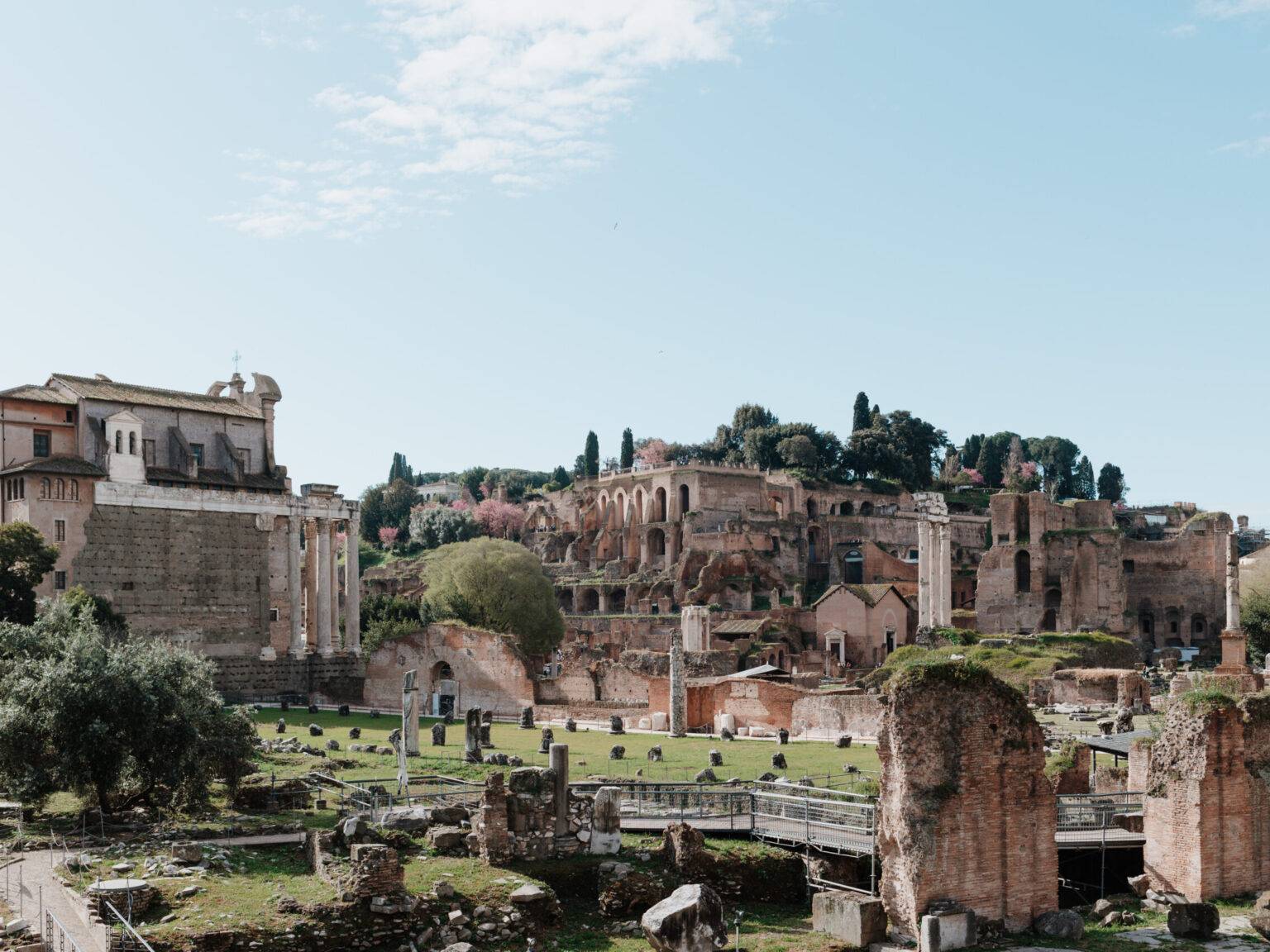 Blick auf das Forum Romanum in Rom mit antiken Ruinen, Säulen und grünen Hügeln im Hintergrund.