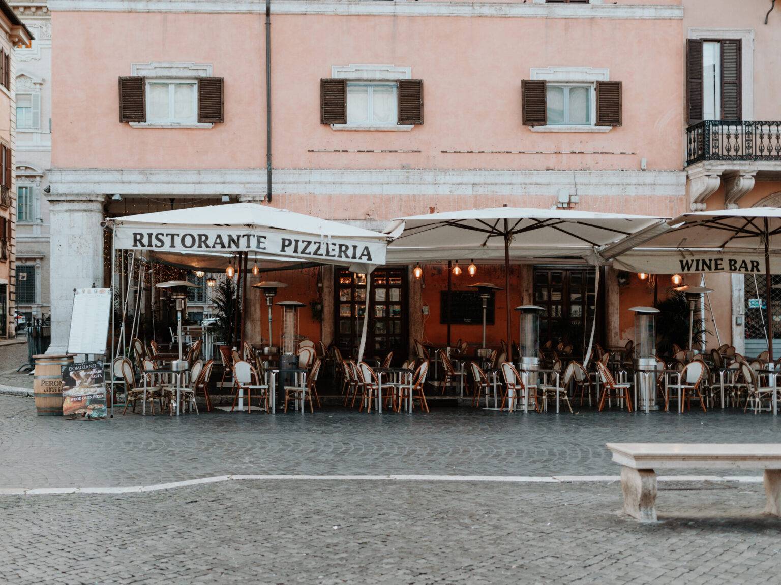 Front eines gemütlichen Restaurants an der Piazza Navona mit gedeckten Tischen unter Sonnenschirmen.