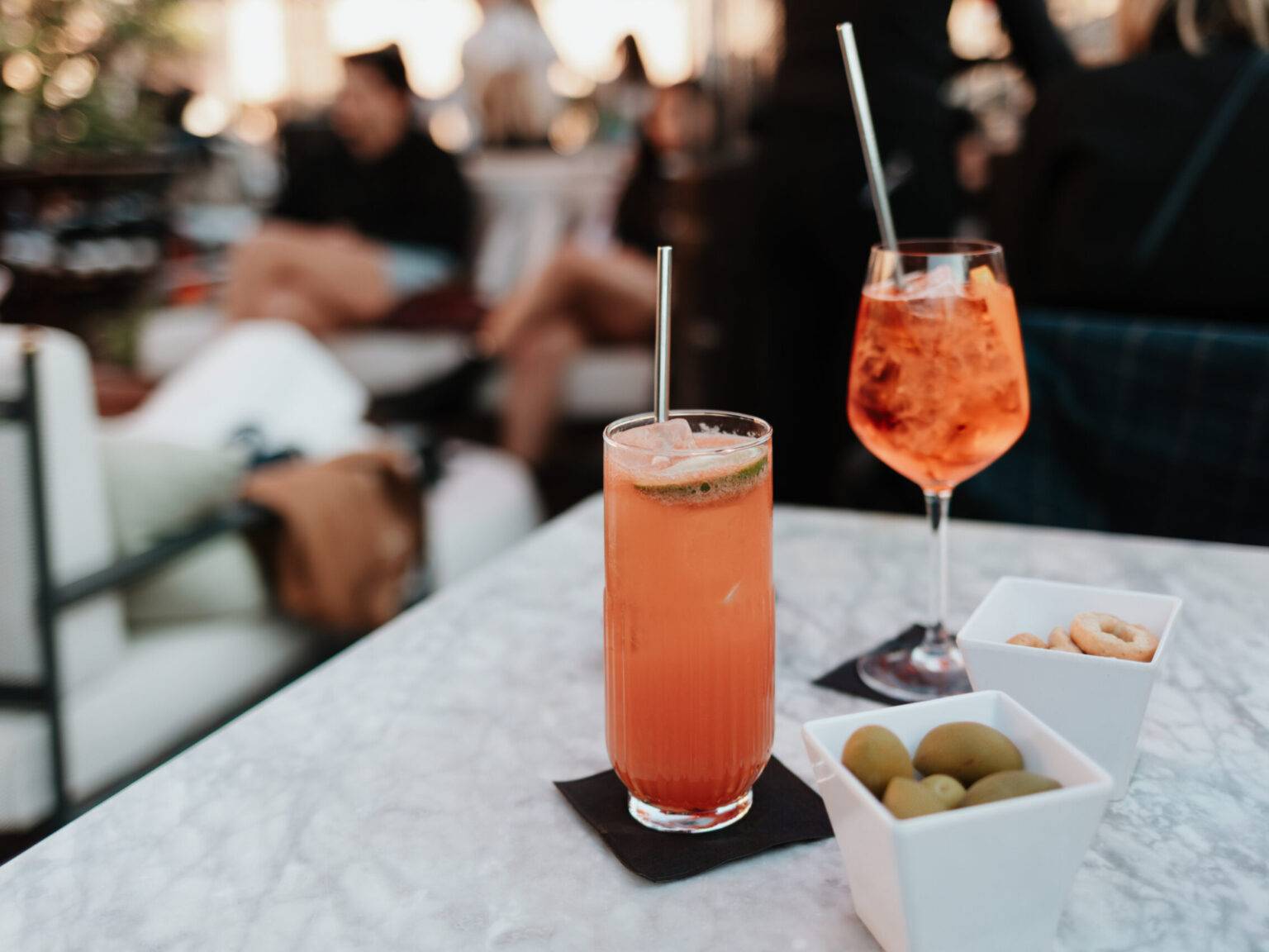 Zwei bunte Aperitif-Cocktails mit Oliven und Snacks auf dem Tisch der Rooftop-Bar.