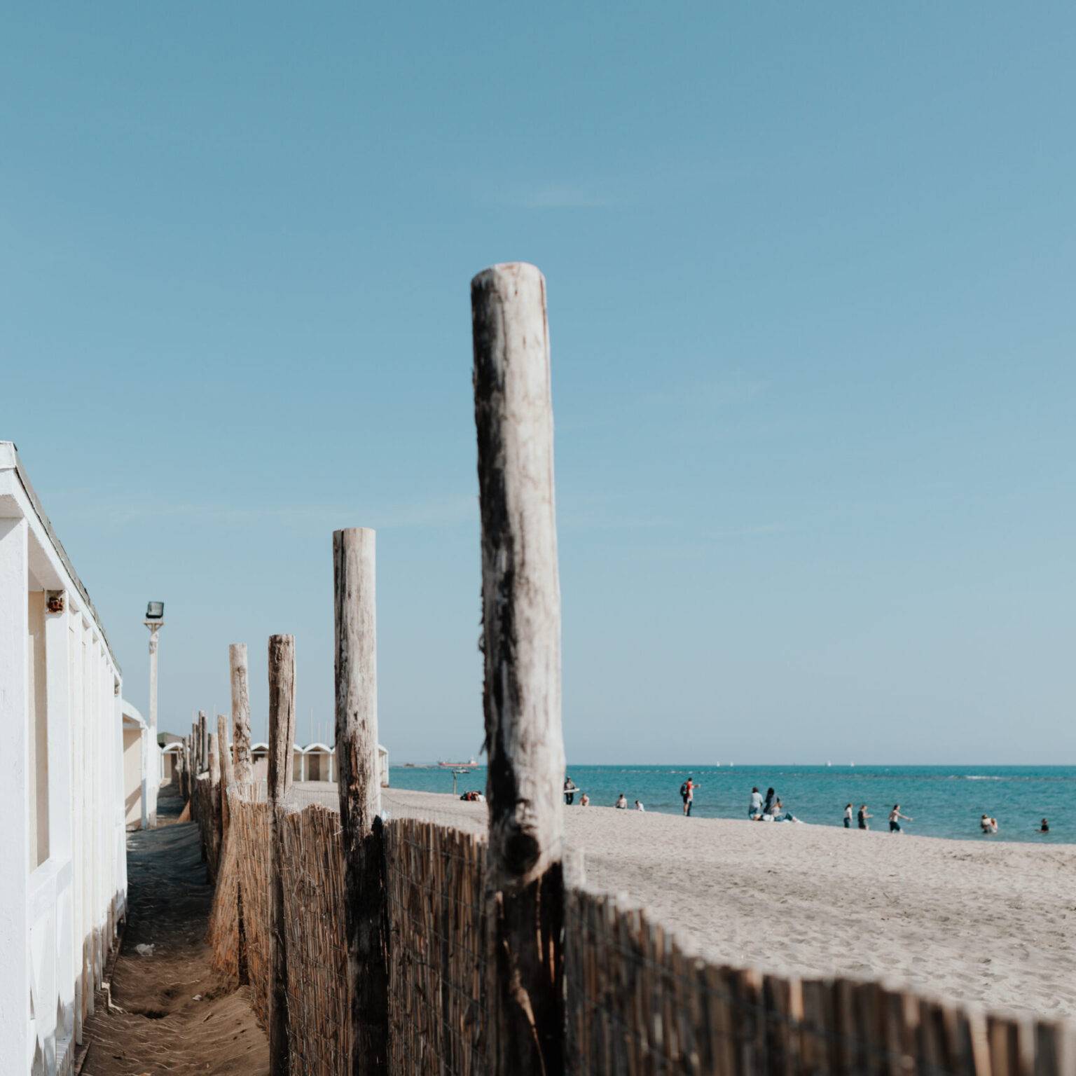 Holzstrandhütten, Sandweg und Badegäste am öffentlichen Strand von Lido di Ostia.