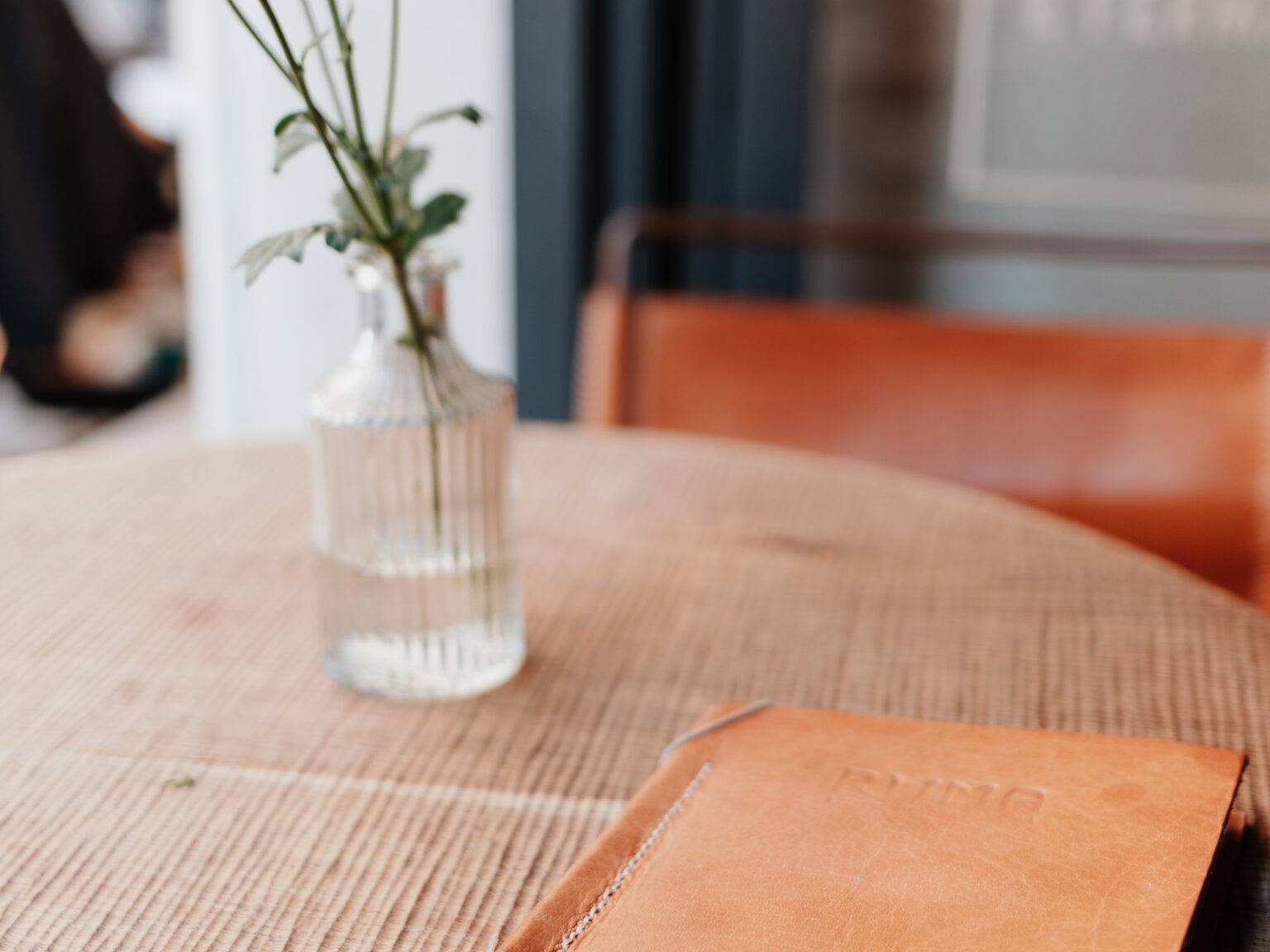Auf einem Tisch im Ruma in Rom liegt eine Speisekarte und daneben steht eine Vase mit Blumen.