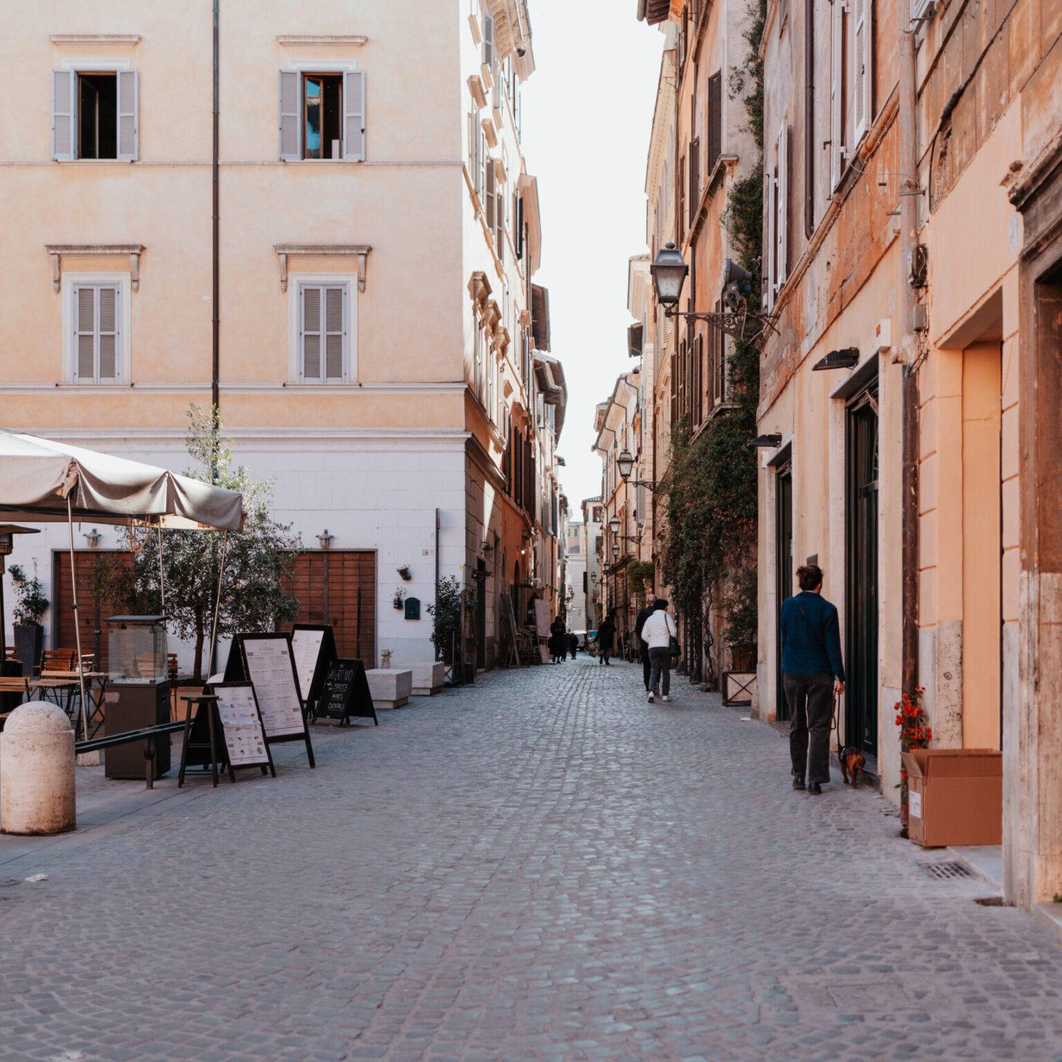 Die Via Coronari in Rom mit Kopfsteinpflaster, Cafés, historischen Fassaden und Passanten.