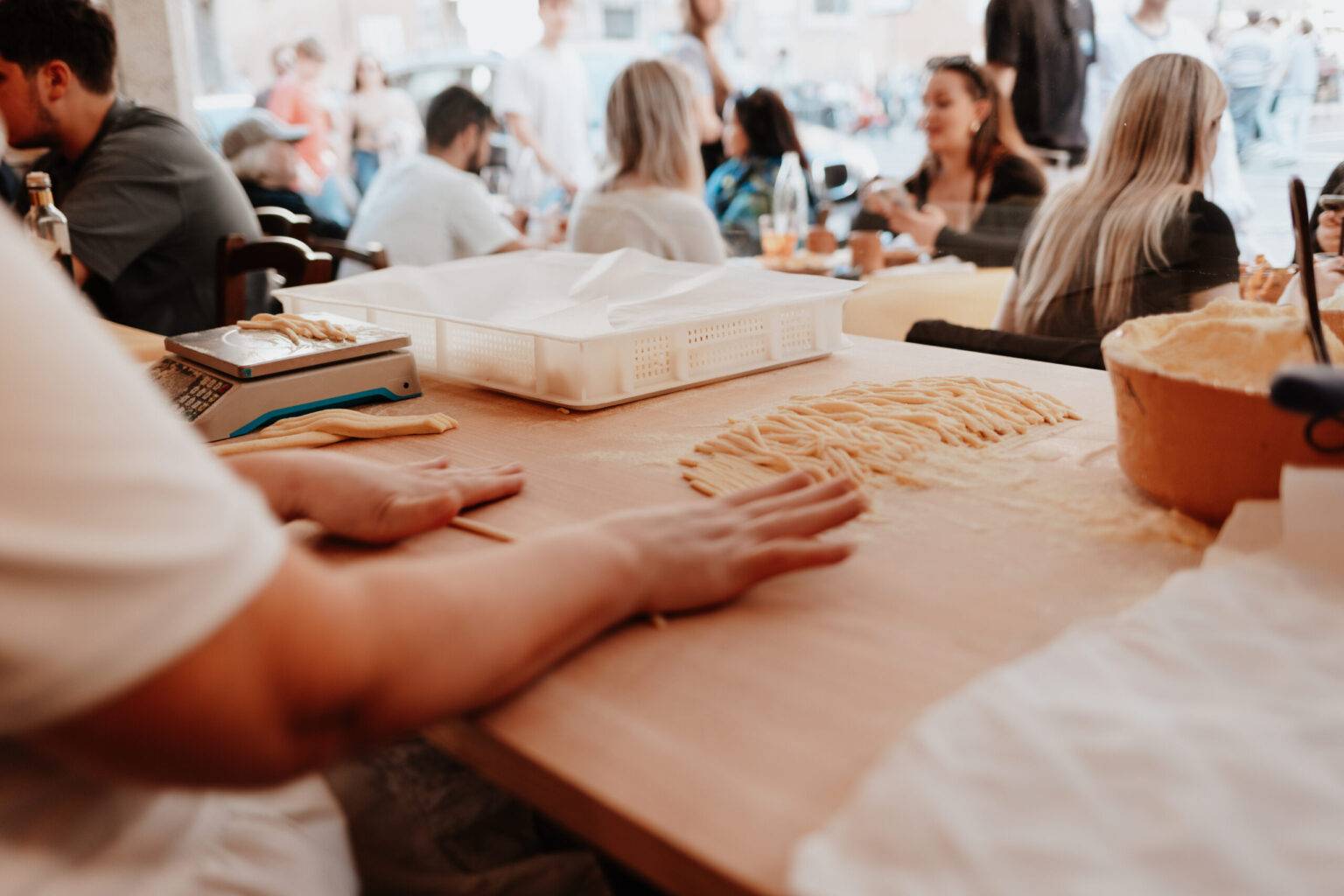 Frische Pasta wird von Hand zubereitet in der Osteria da Fortunata in Rom, Gäste sitzen im Hintergrund.