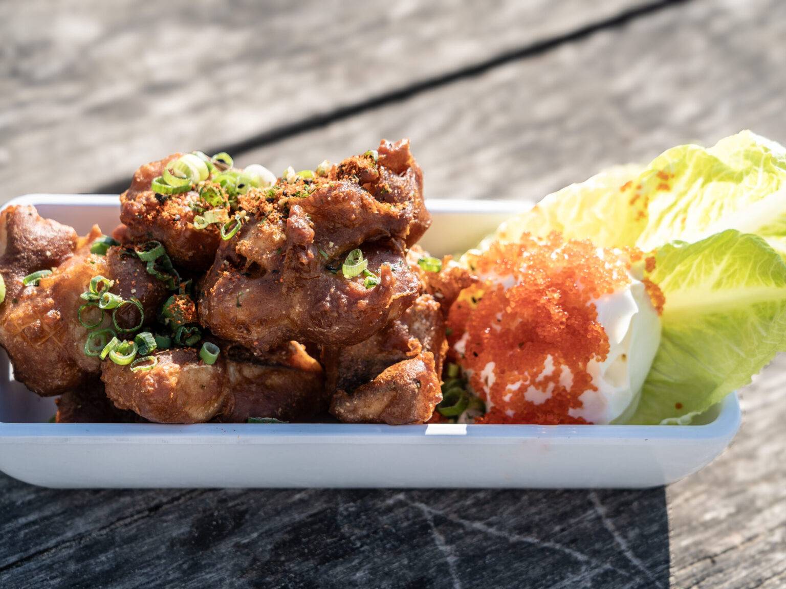 Eine Schale mit Kibbeling, einem Dip und zwei Salatblättern.