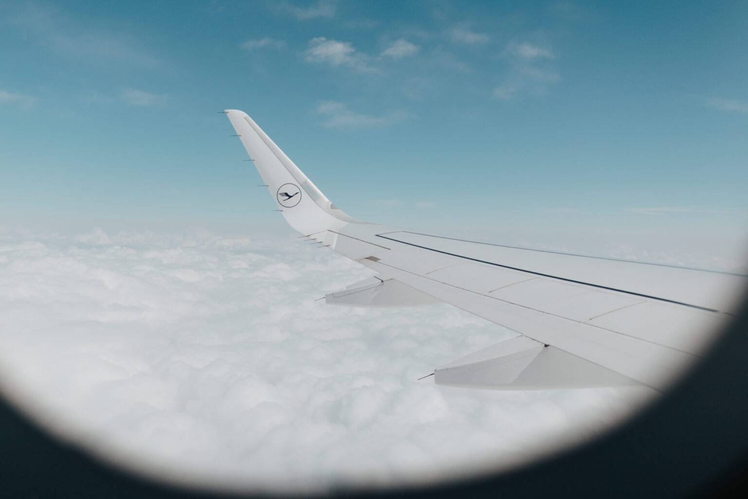 Die Tragfläche eines Lufthansa-Flugzeugs über den Wolken bei blauem Himmel.