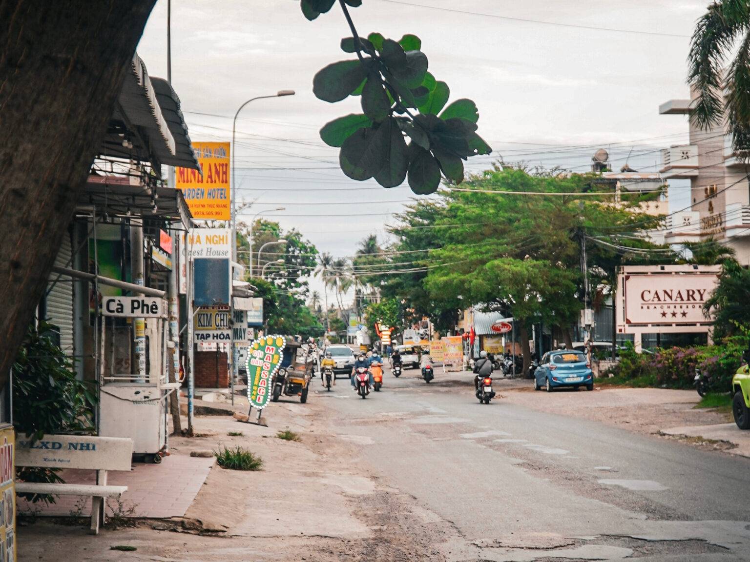 Eine asphaltierte Straße in Mui Ne mit Rollern und Häusern links und rechts.