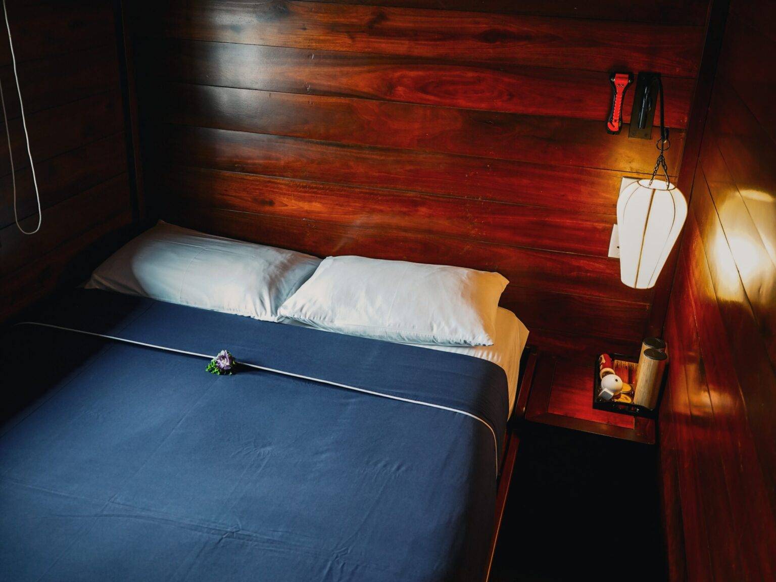Eine Kabine auf der Basaac 2 mit einem Doppelbett, einem Nachtisch mit Lampe und mit dunklem Holz vertäfelten Wänden.