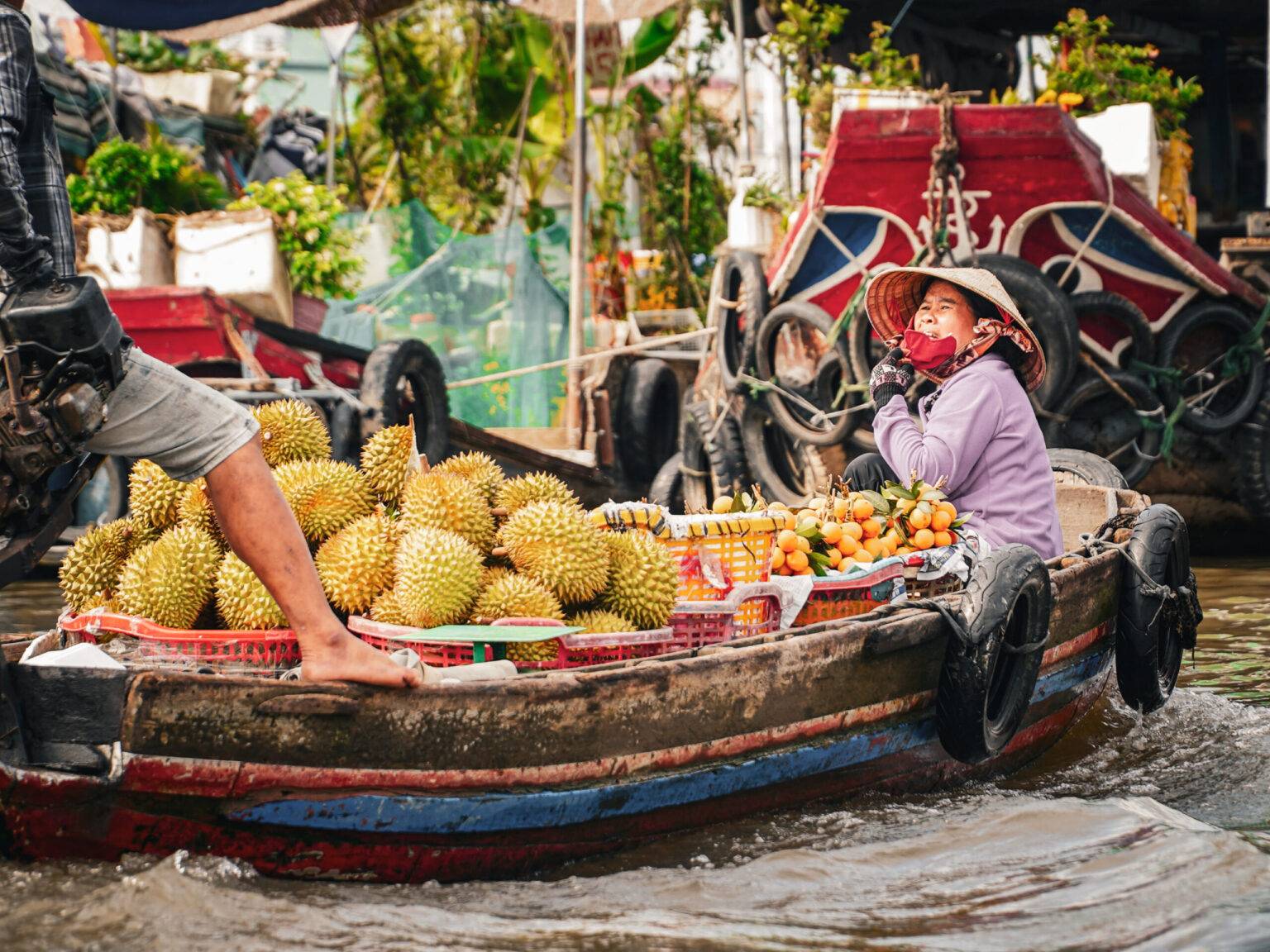 Ein Boot mit einer Händlerin vollgeladen mit Durian Früchten auf dem schwimmenden Markt Cai Rang.