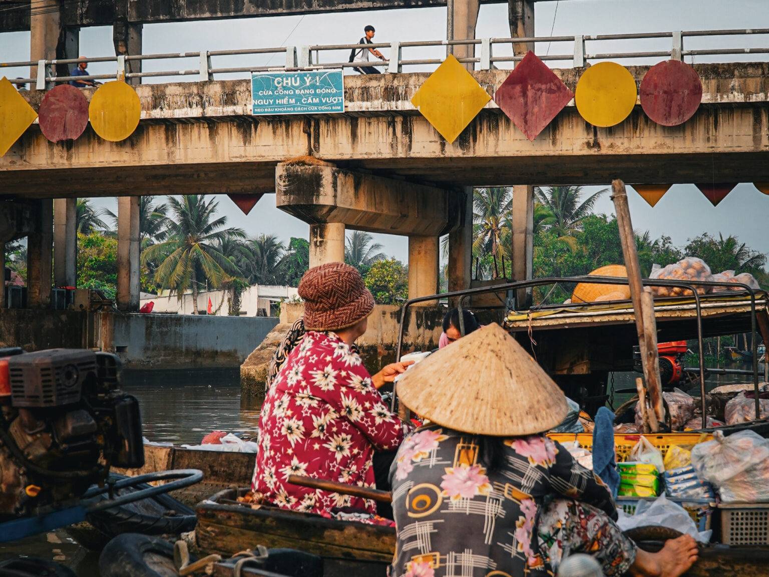 Menschen auf dem schwimmenden Markt Phong Dien unter einer Brücke auf Holzbooten.