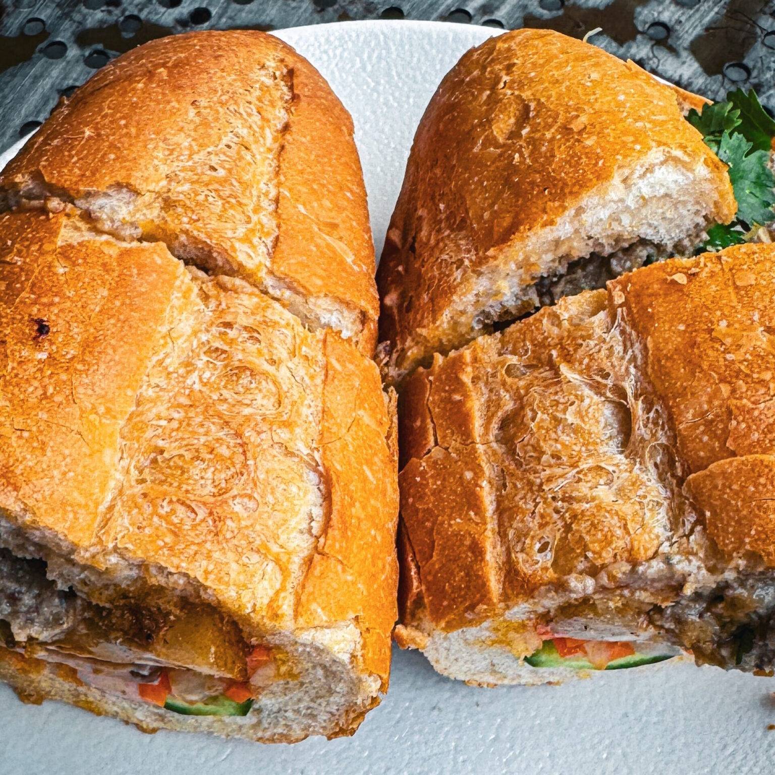 Auf einem Teller liegt ein aufgeschnittenes Banh Mi Sandwich.
