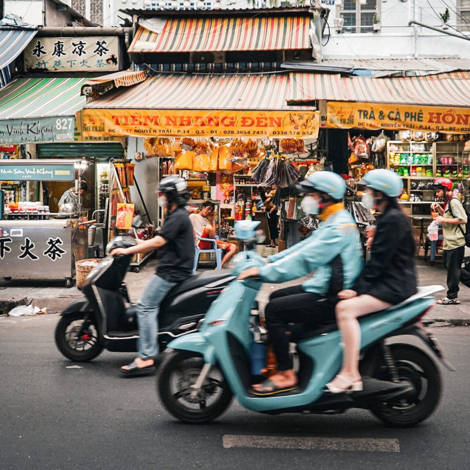 Eine Straßenszene in Cholon in Ho Chi Minh City mit bunten Verkaufsständen und vorbeifahrenden Rollern.