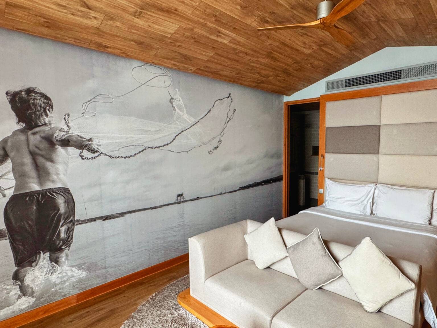 Ein Zimmer im Fusion Suites mit einem hellen Sofa, einem Doppelbett und einem großen Mural von einem Fischerjungen an der Wand.