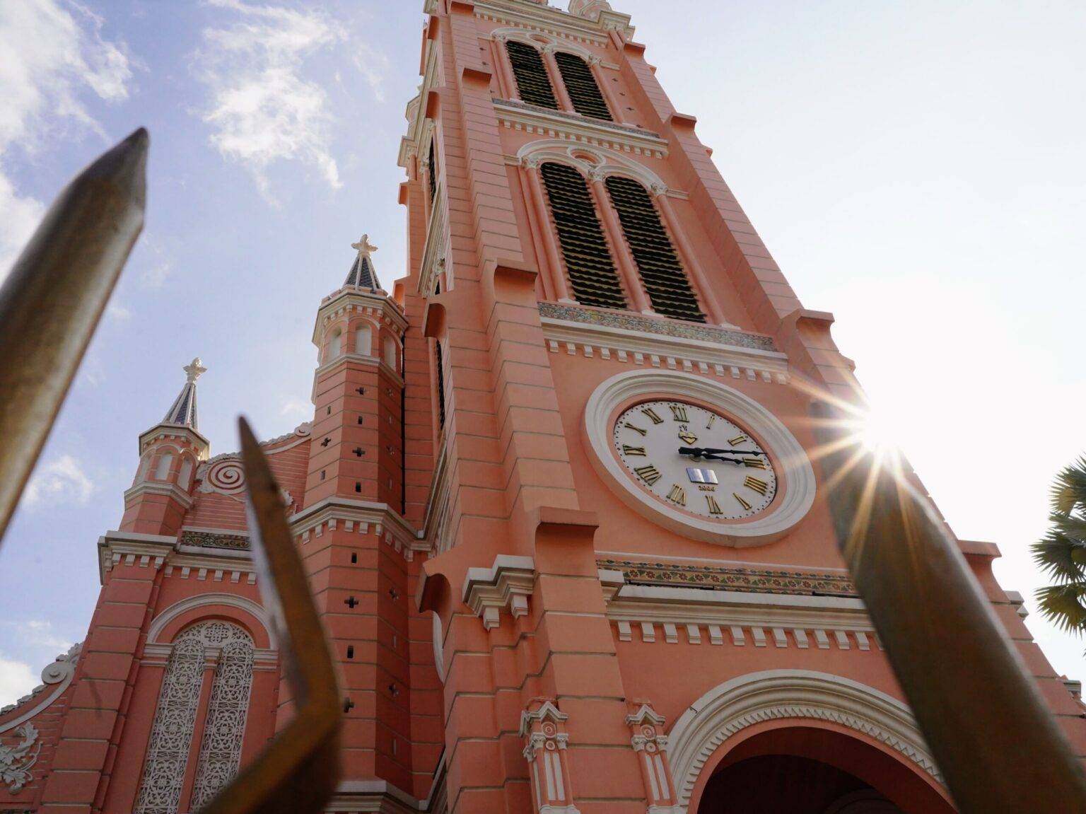 Die rosafarbene Fassade der Pink Church in Ho Chi Minh City mit einem zentralen hohen Turm und einer großen Uhr.