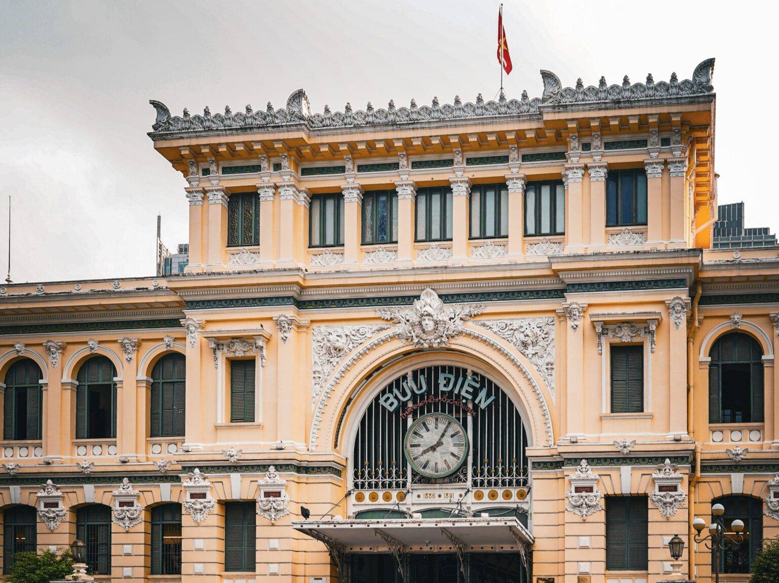 Die gelbe Fassade des Postamts in Ho Chi Minh City mit weißen Verzierungen und einer großen Uhr.