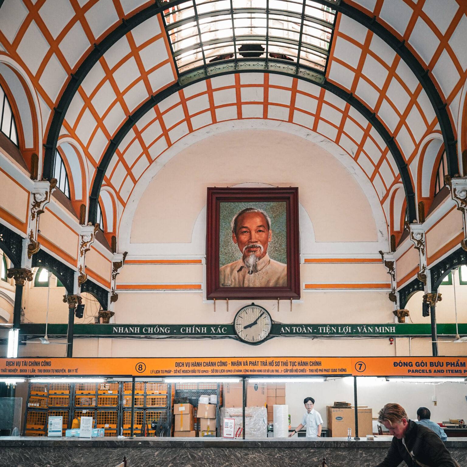 Die Halle des Postamts von Ho Chi Minh City von innen mit einer hohen, gewölbten Decke, einigen Schaltern und einem großen Portrait von Ho Chi Minh.