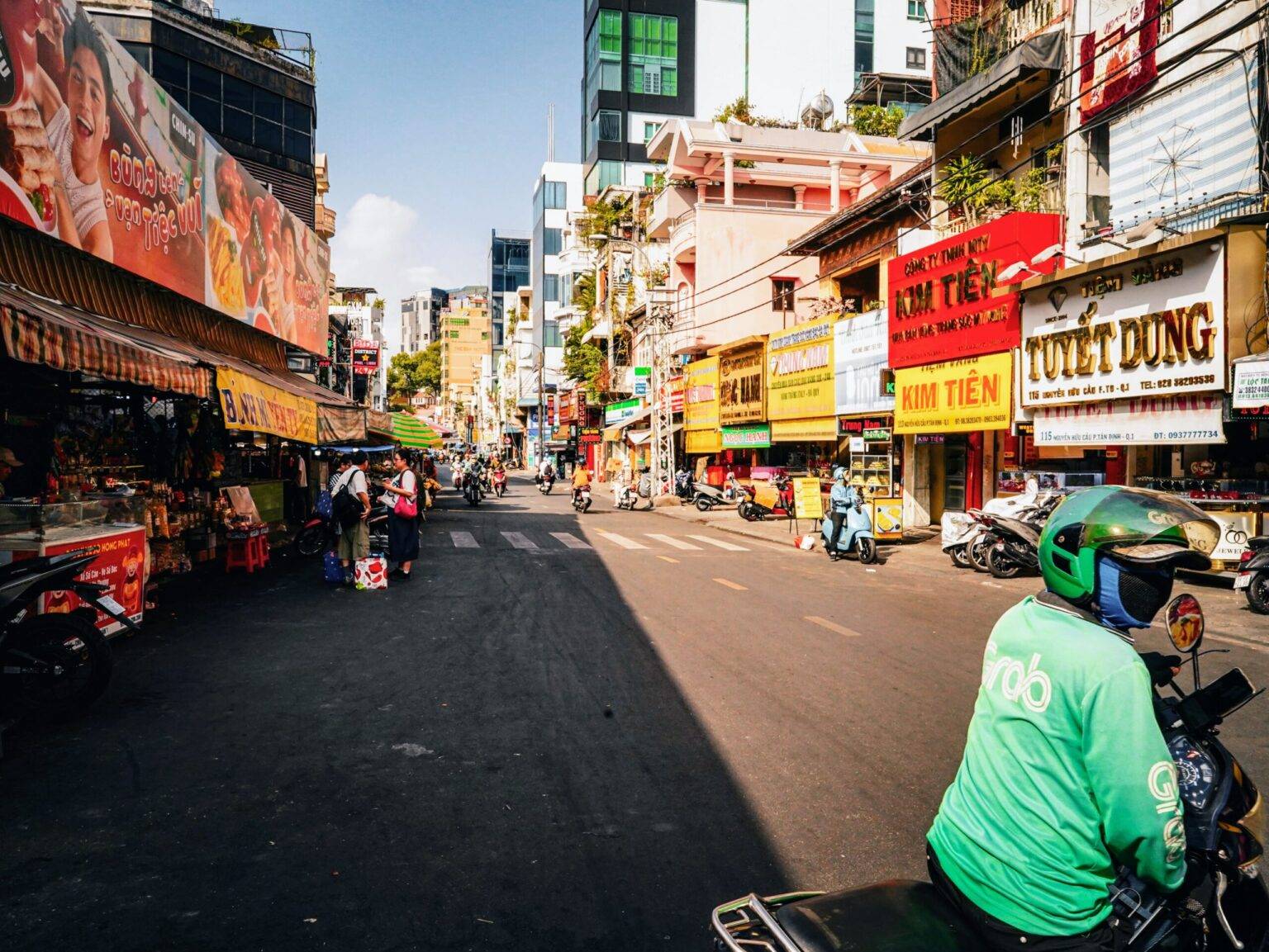 Eine Straße in Ho Chi Minh City mit bunten Ladenfronten, Passanten und Rollerfahrern.