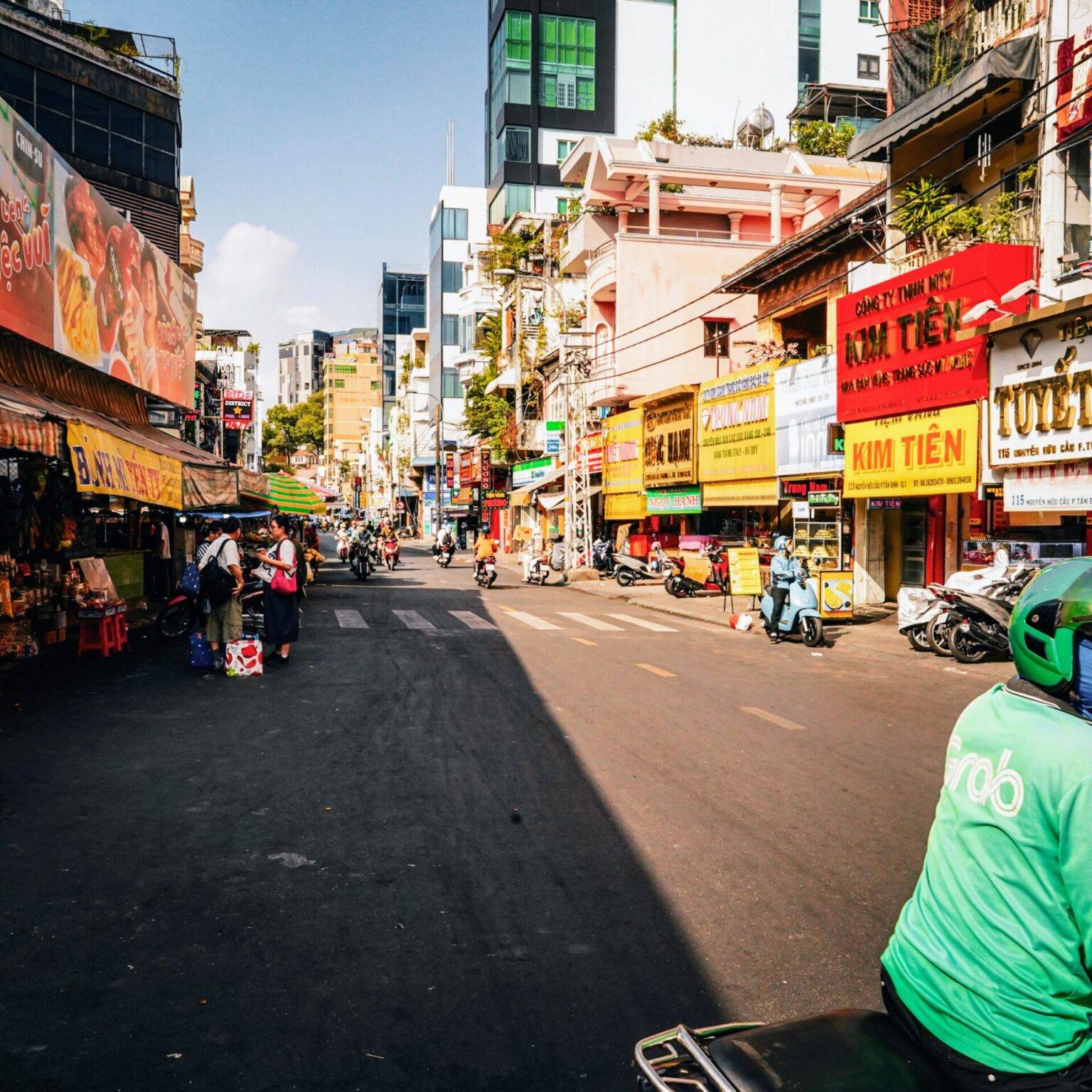 Eine Straße in Ho Chi Minh City mit bunten Ladenfronten, Passanten und Rollerfahrern.