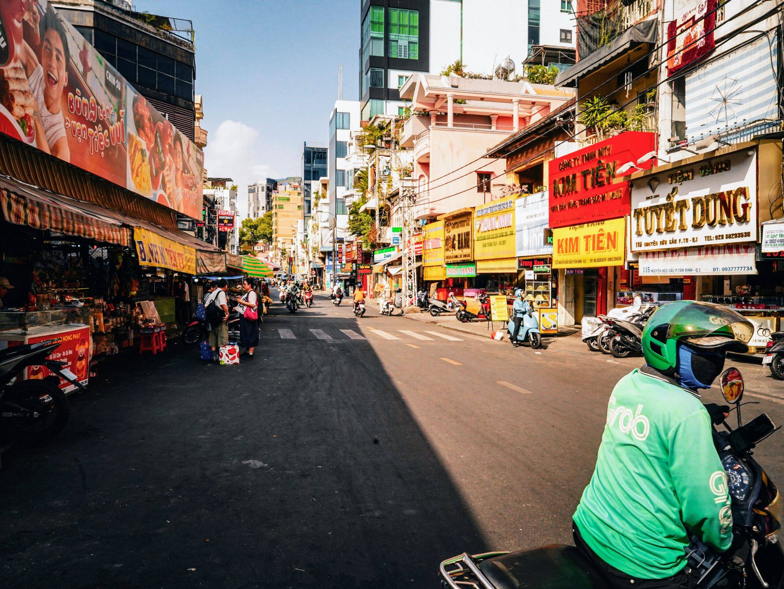 Eine Straße in Ho Chi Minh City mit bunten Ladenfronten, Passanten und Rollerfahrern.