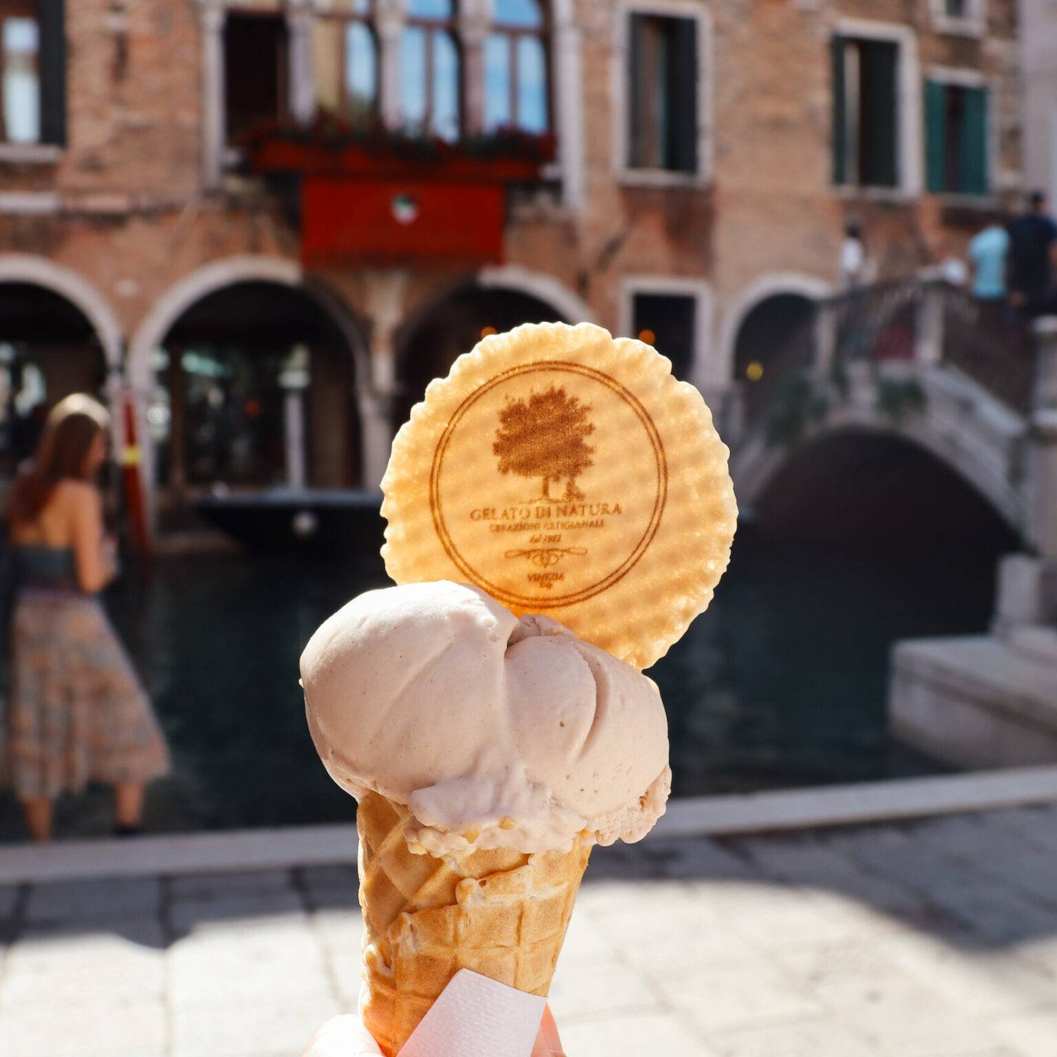 Eine Waffel mit zwei Kugeln Eis. Im Hintergrund eine Gasse in Venedig.