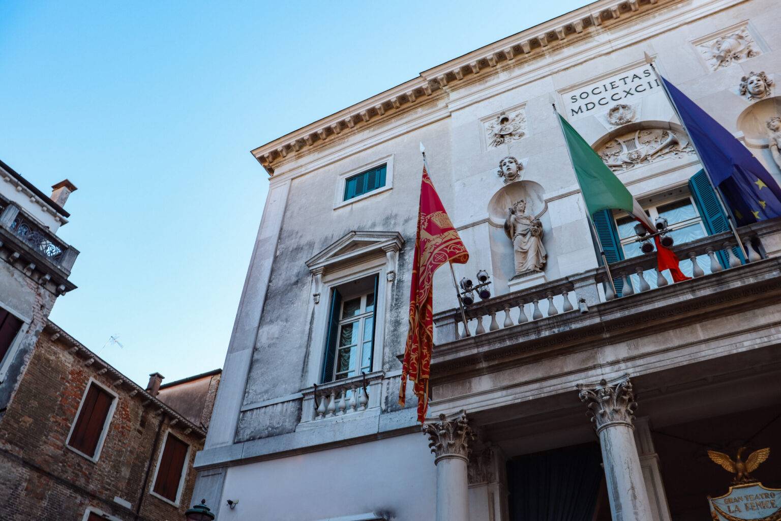 Die Fassade des Teatro La Fenice in Venedig mit einem Balkon und mehreren Flaggen.