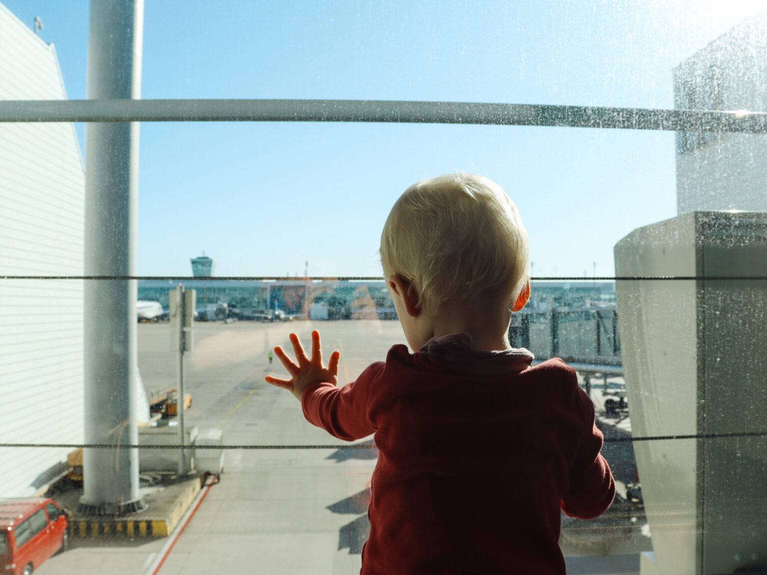 Ein Kind von hinten an der Scheibe mit Blick auf das Rollfeld.
