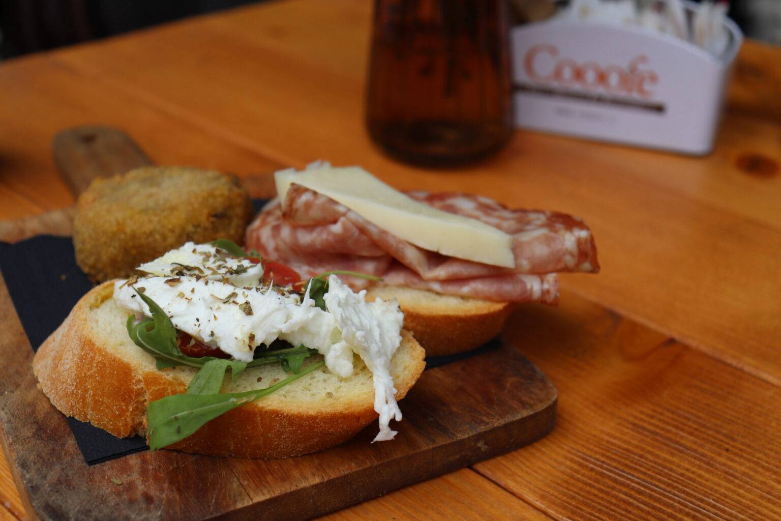 Zwei Cicchetti, einmal mit Salami und eine vegetarische Variante mit Tomate und Käse auf einem Holzbrett.