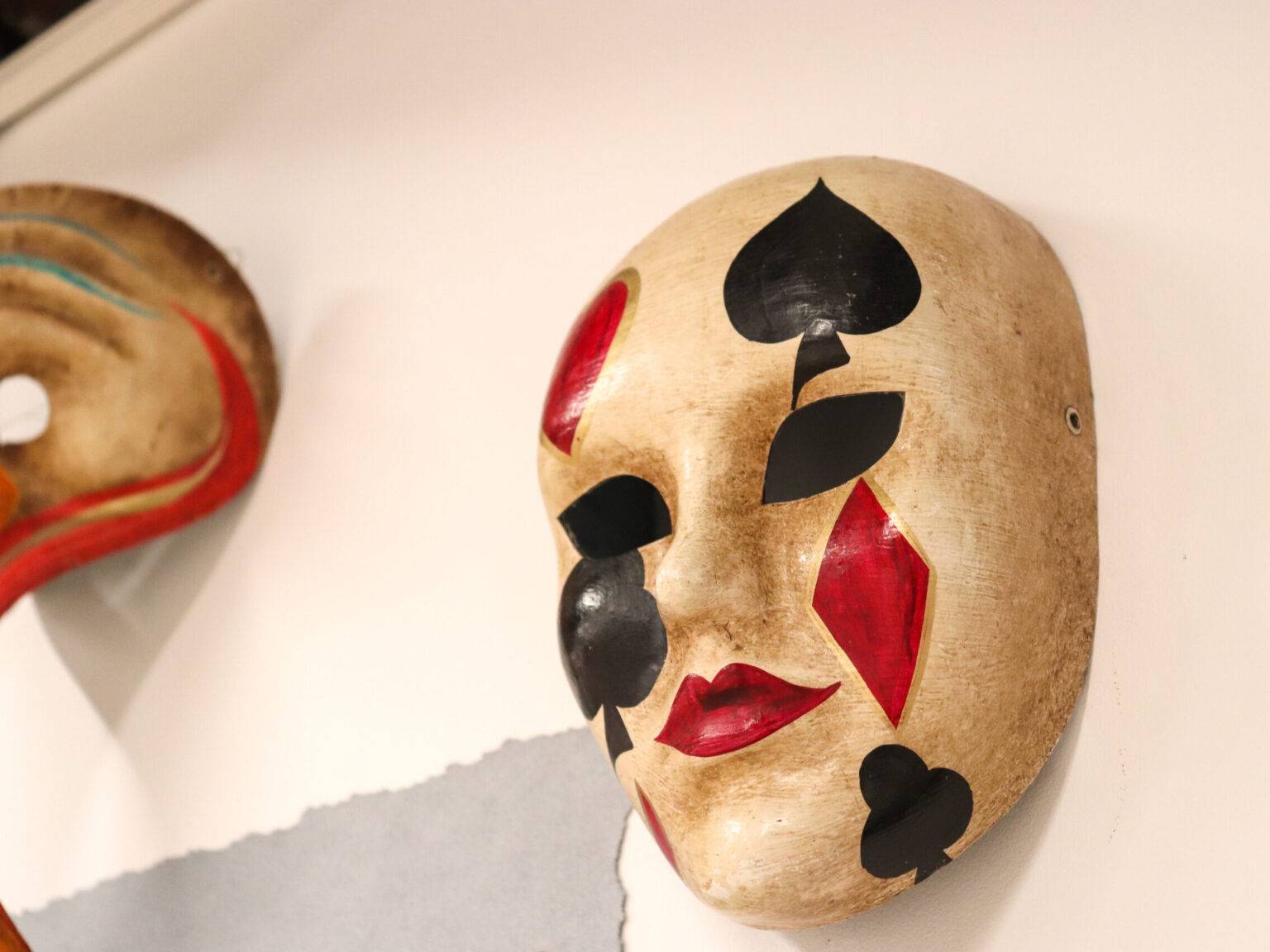 Maske mit Spielkarten-Symbolen an der Wand eines Ateliers, in dem man Masken bemalen kann.