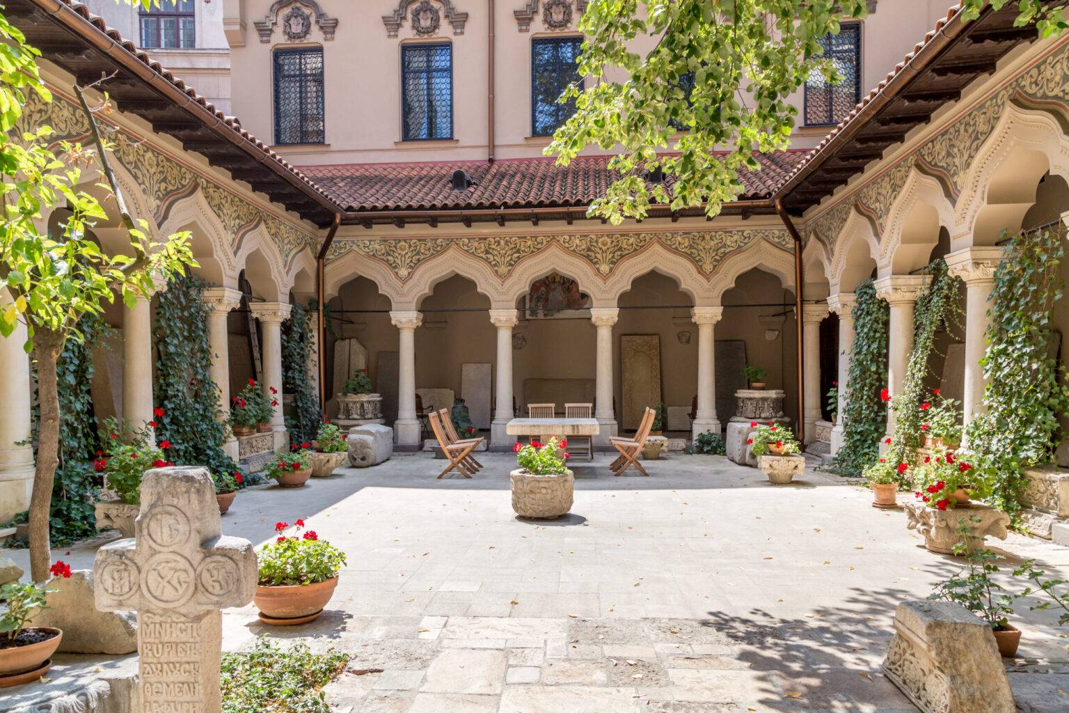 Der Innenhof des Klosters Stavropoleos in Bukarest mit vielen mit Efeu bewachsenen Säulen, spitz zulaufenden Torbögen und detaillierten Verzierungen.