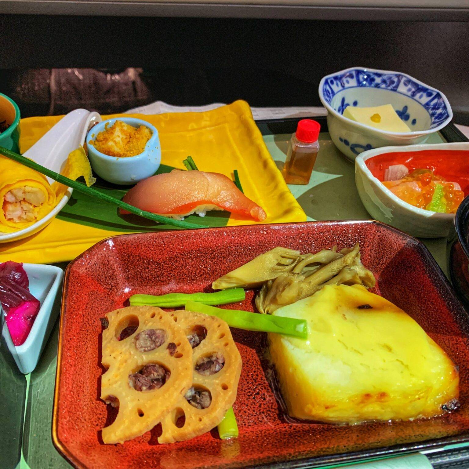 Teller und Bowls mit verschiedenen Speisen, darunter Fisch, Tofu und Gemüse.