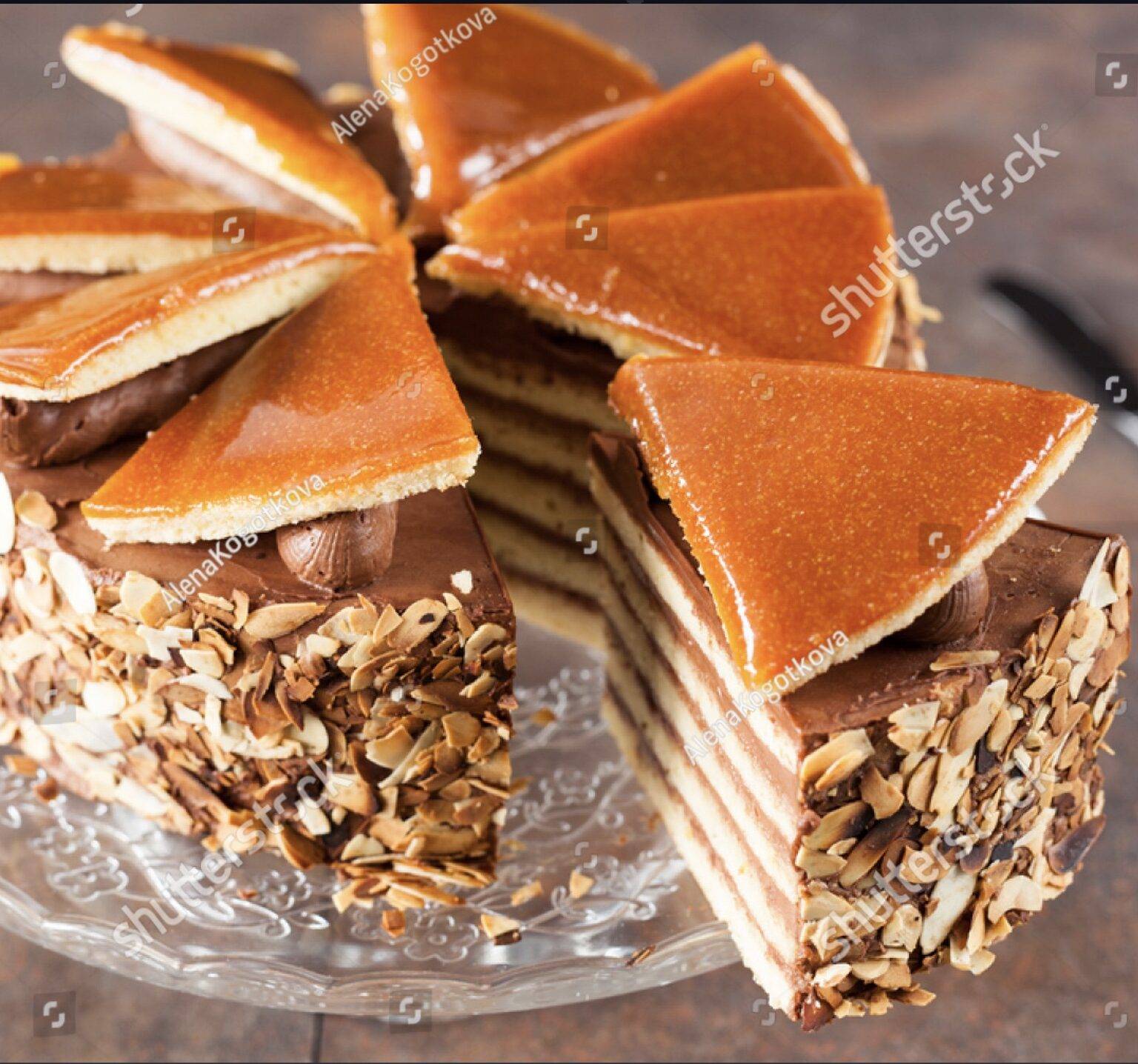 Eine Dobostorte mit Schichten aus Biskuit und Schokoladencreme und einer Karamelhaube auf einem gläsernen Servierteller.