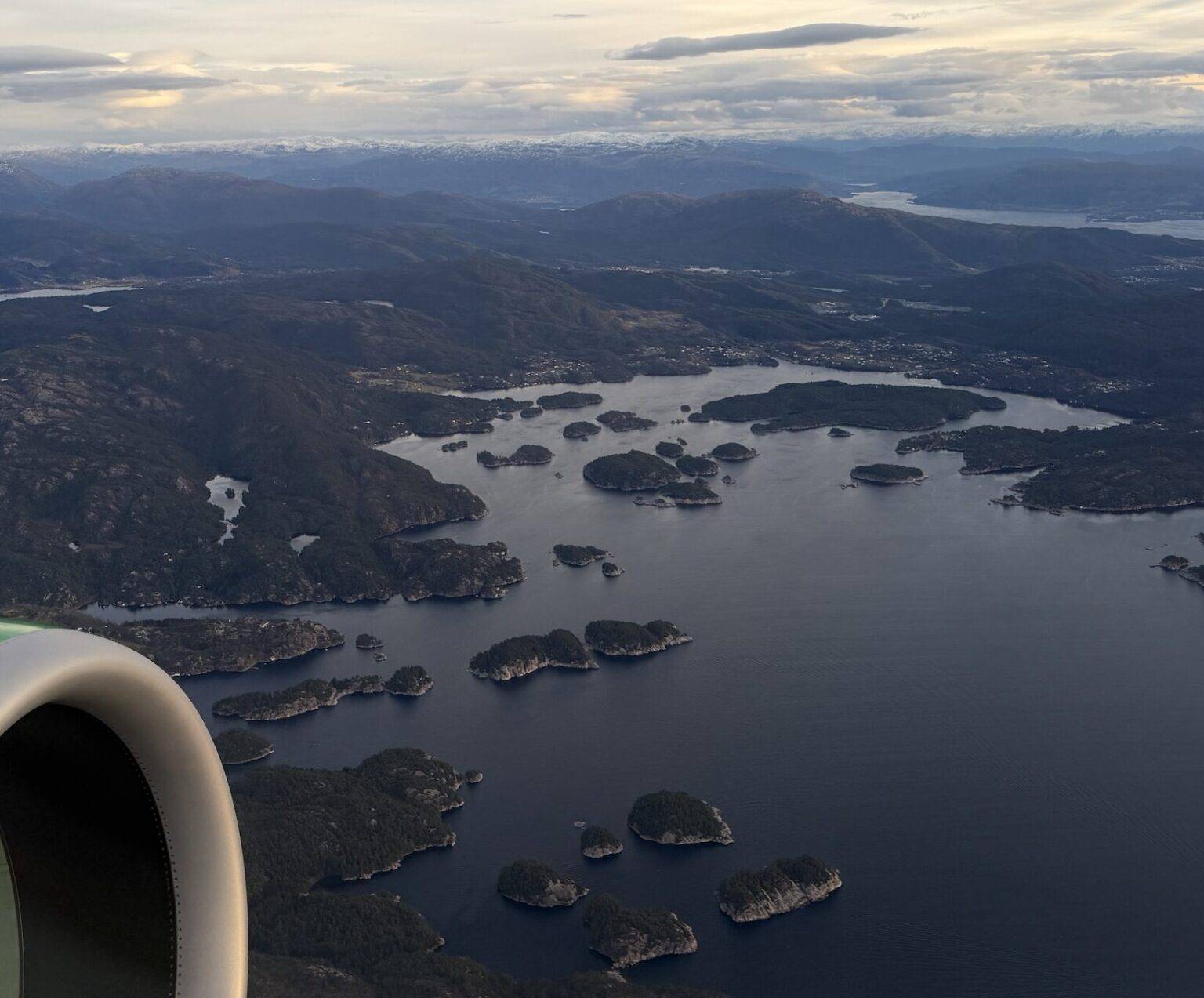 Blick aus einem Flugzeugfenster auf Fjorde mit Triebwerk.