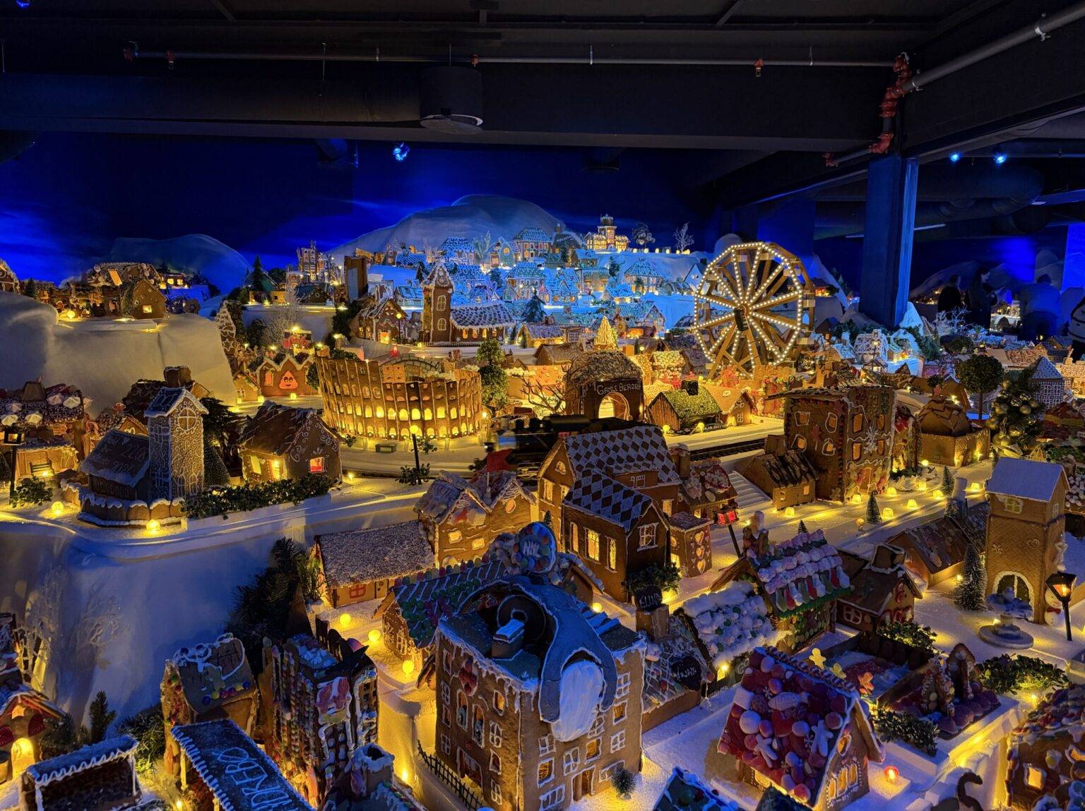 Bunte, beleuchtete Weihnachtsdorf-Szene mit vielen Häusern, einem Riesenrad und schneebedeckten Landschaften (alles aus Pfefferkuchen).