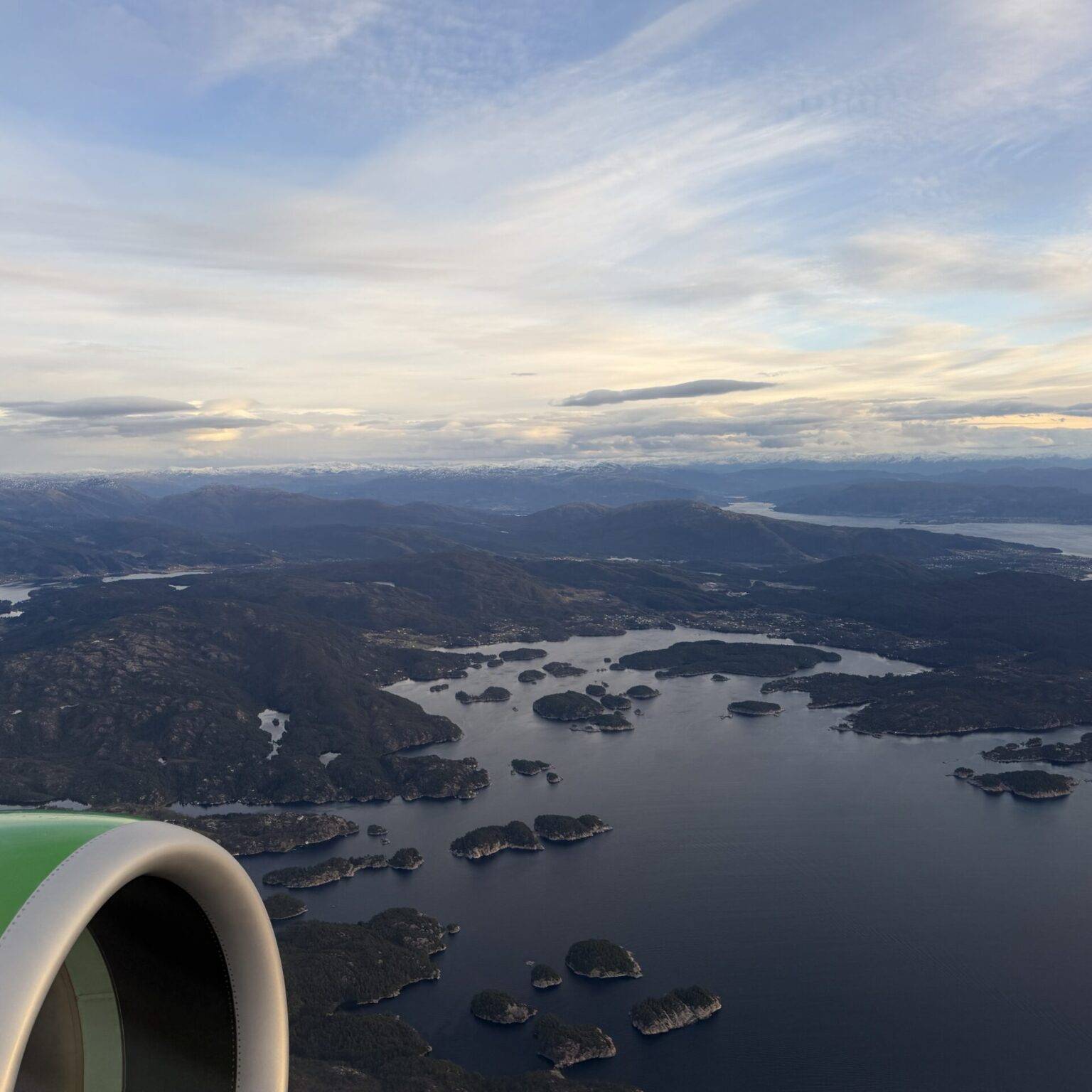 Luftaufnahme eines Küstengebiets mit Inseln und Wasser, im Vordergrund ein Flugzeugtriebwerk.