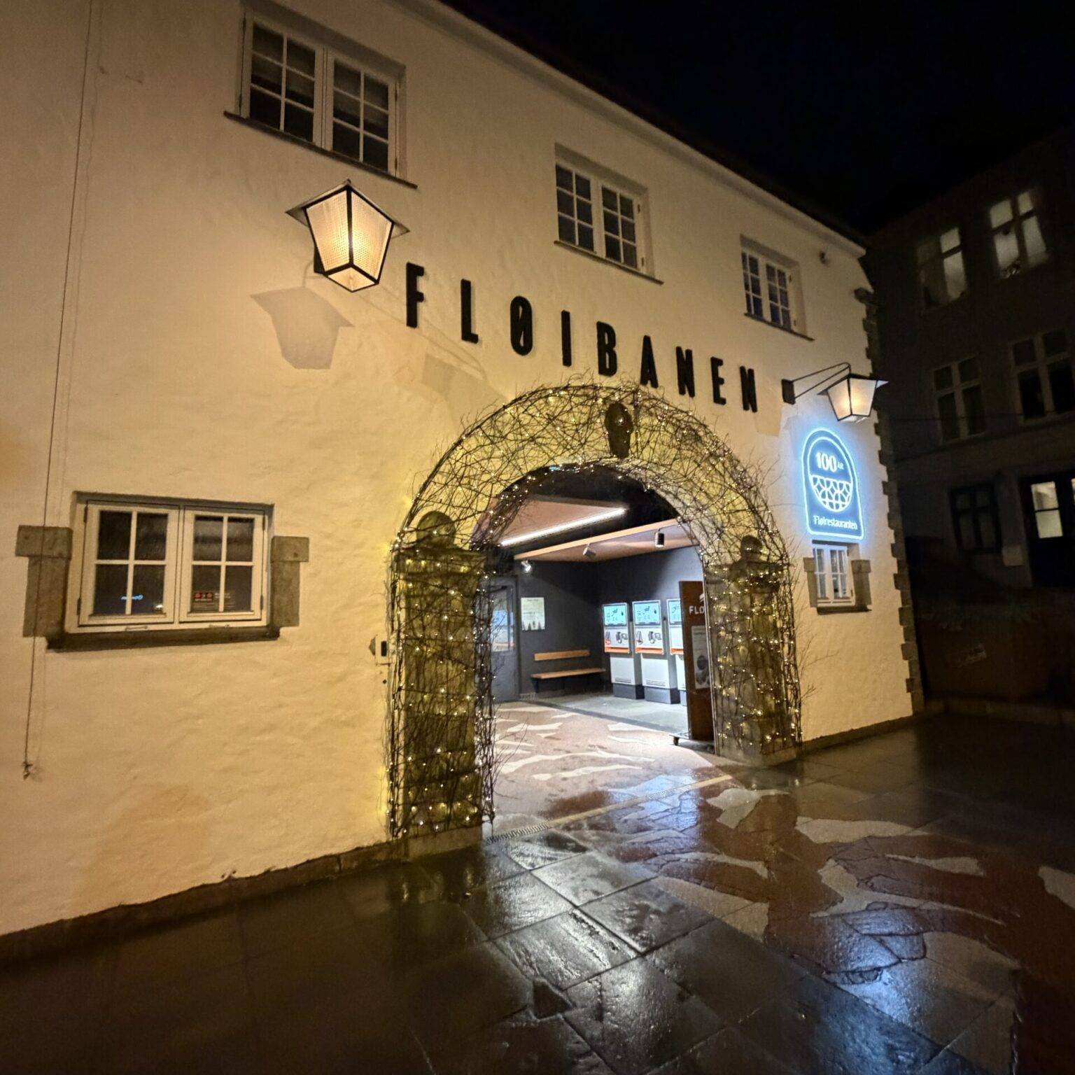 Zugang zur Fløibanen in einem Altstadtgebäude in Bergen, Laterne über dem Tor, dunkler Himmel im Hintergrund.