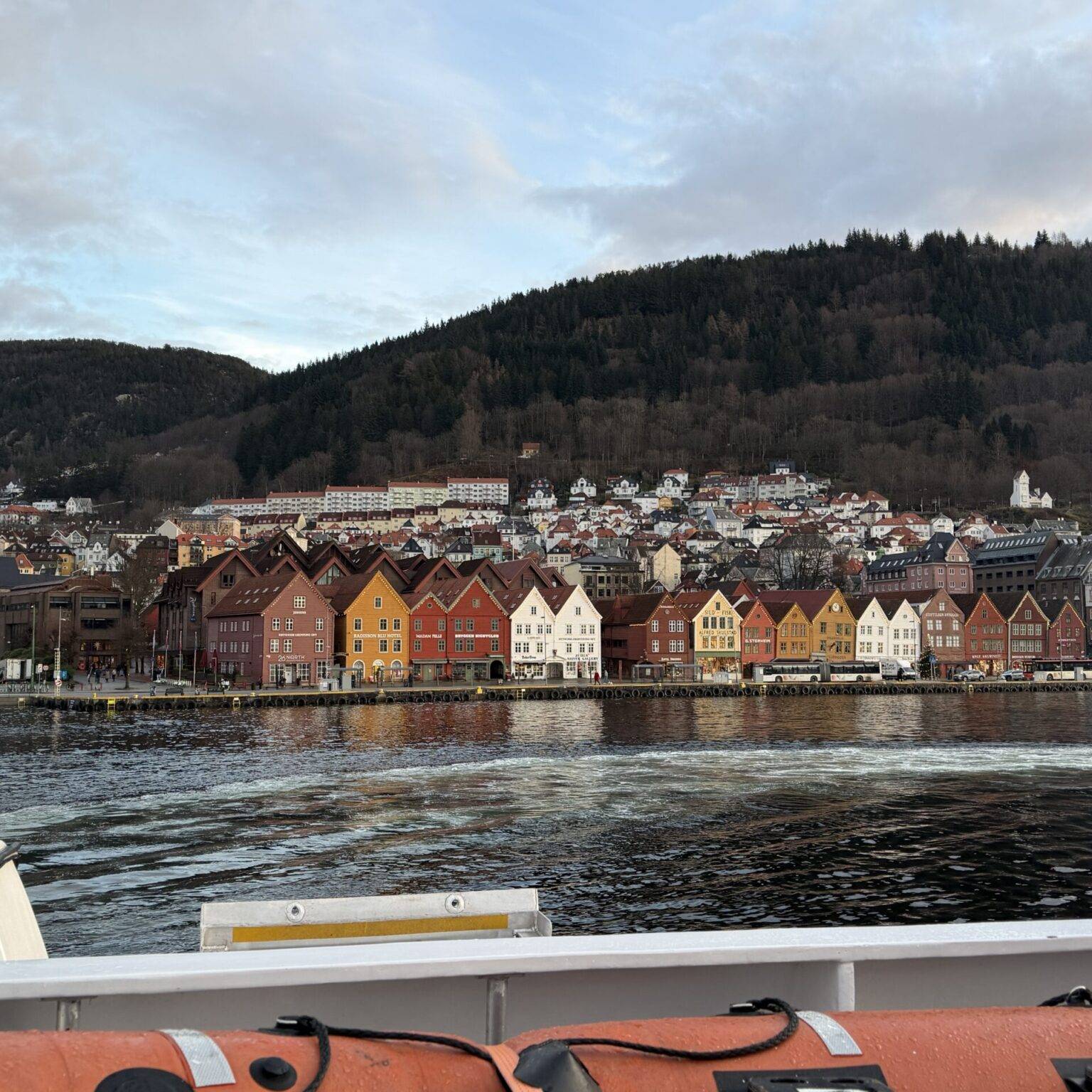 Farbenfrohe Häuserreihe am Ufer von Bergen, aufgenommen vom Wasser mit Bootselementen im Vordergrund.