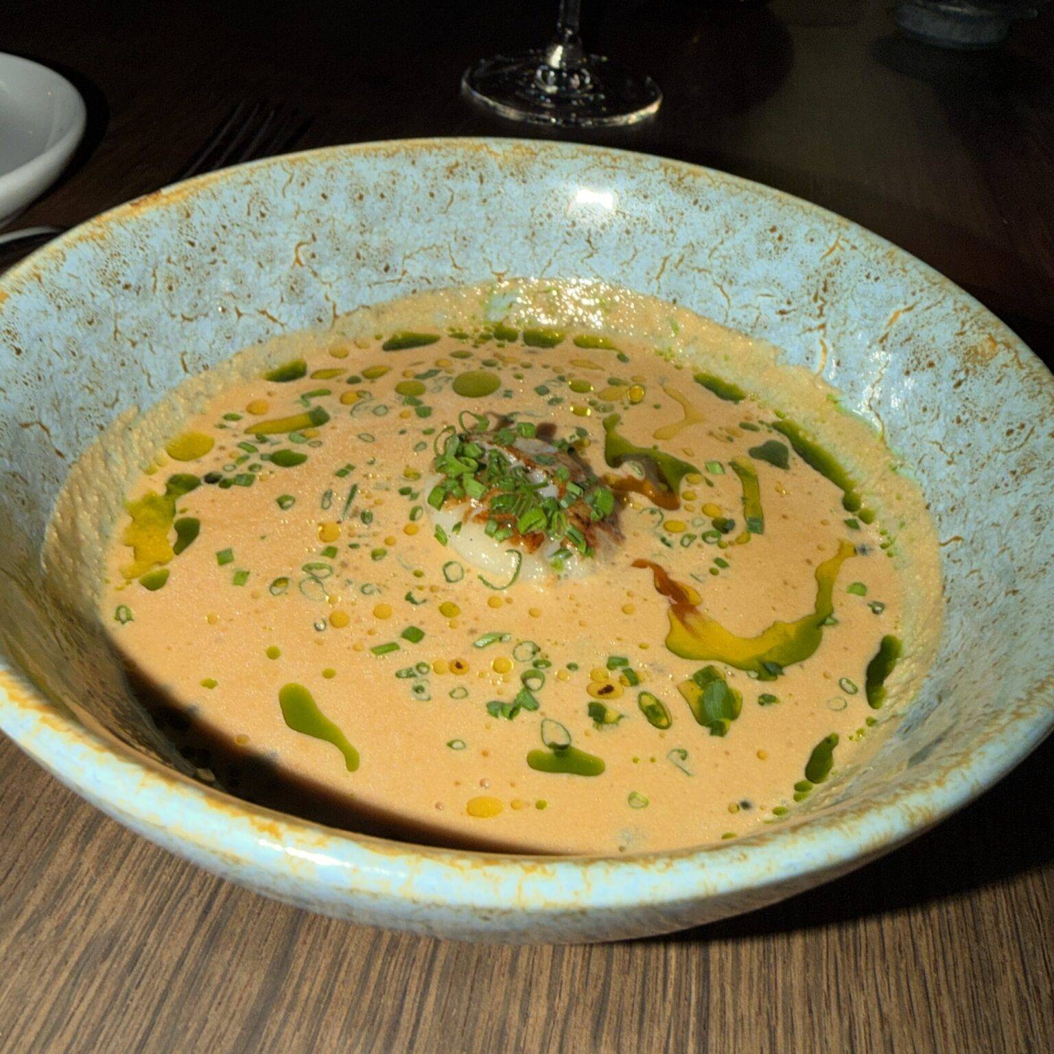 Eine Schüssel mit cremiger Fischsuppe, garniert mit Kräutern, auf einem Holztisch.