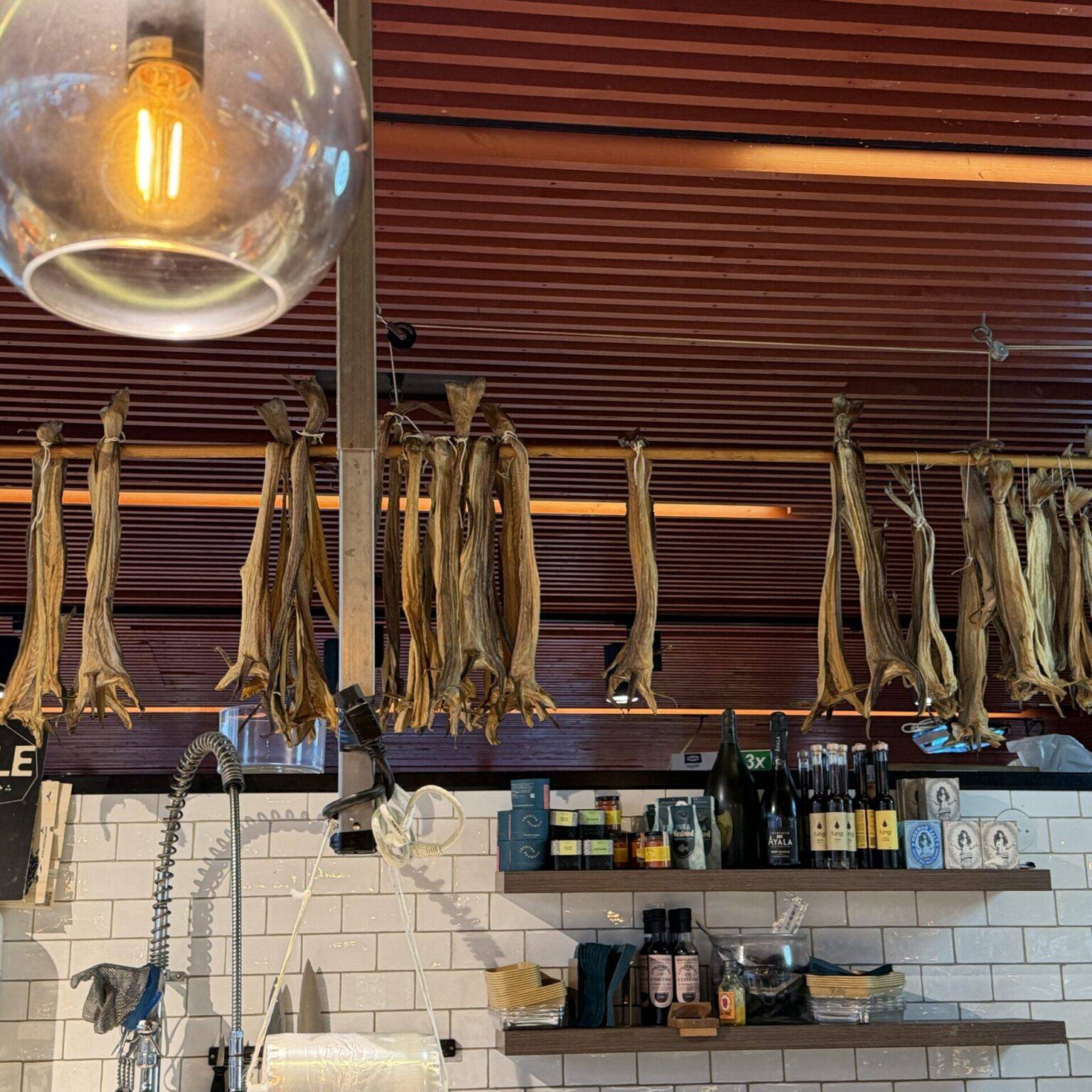 Hängende Stockfische und eine gläserne Deckenleuchte in einem Fischimbiss.