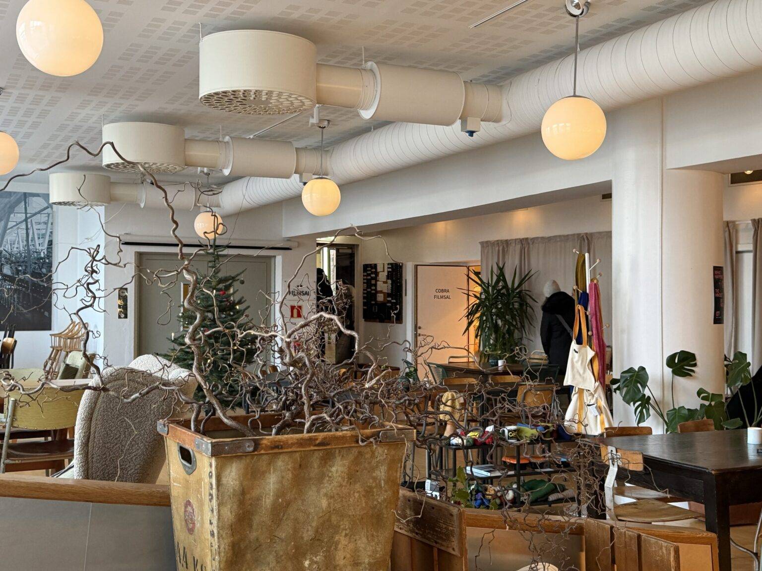 Cafébereich im Salhus Textilmuseum mit Pflanzen, Lampen und gemütlicher Atmosphäre.