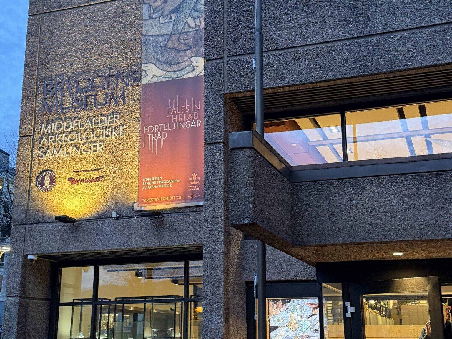 Eingang des Bryggen Museum in Bergen mit Glasfront, Treppe im Inneren und Banner an der Fassade.