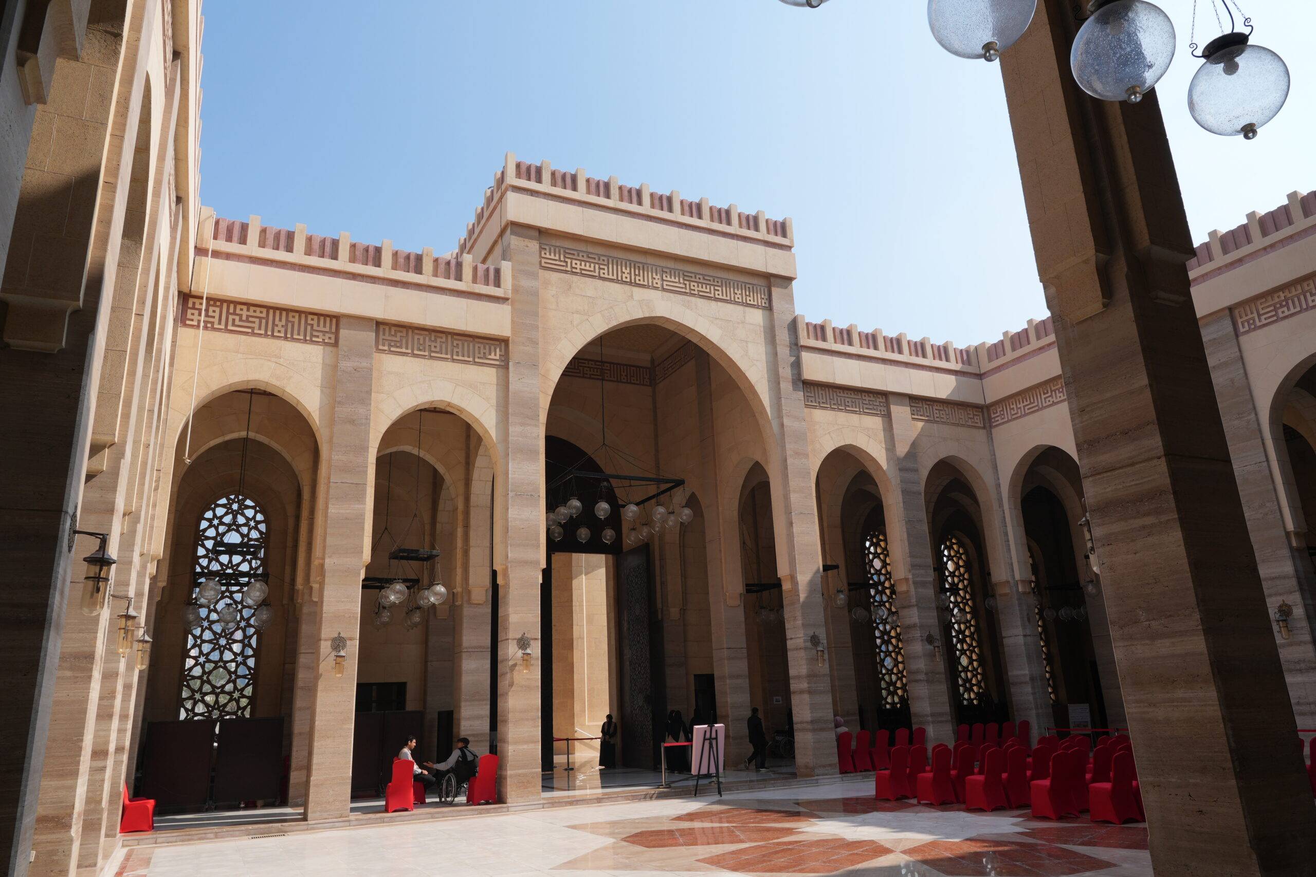 Säulengang im Innenhof der Al Fateh Grand Mosque in Manama, mit kunstvollen Bogenfenstern und Mosaikboden.